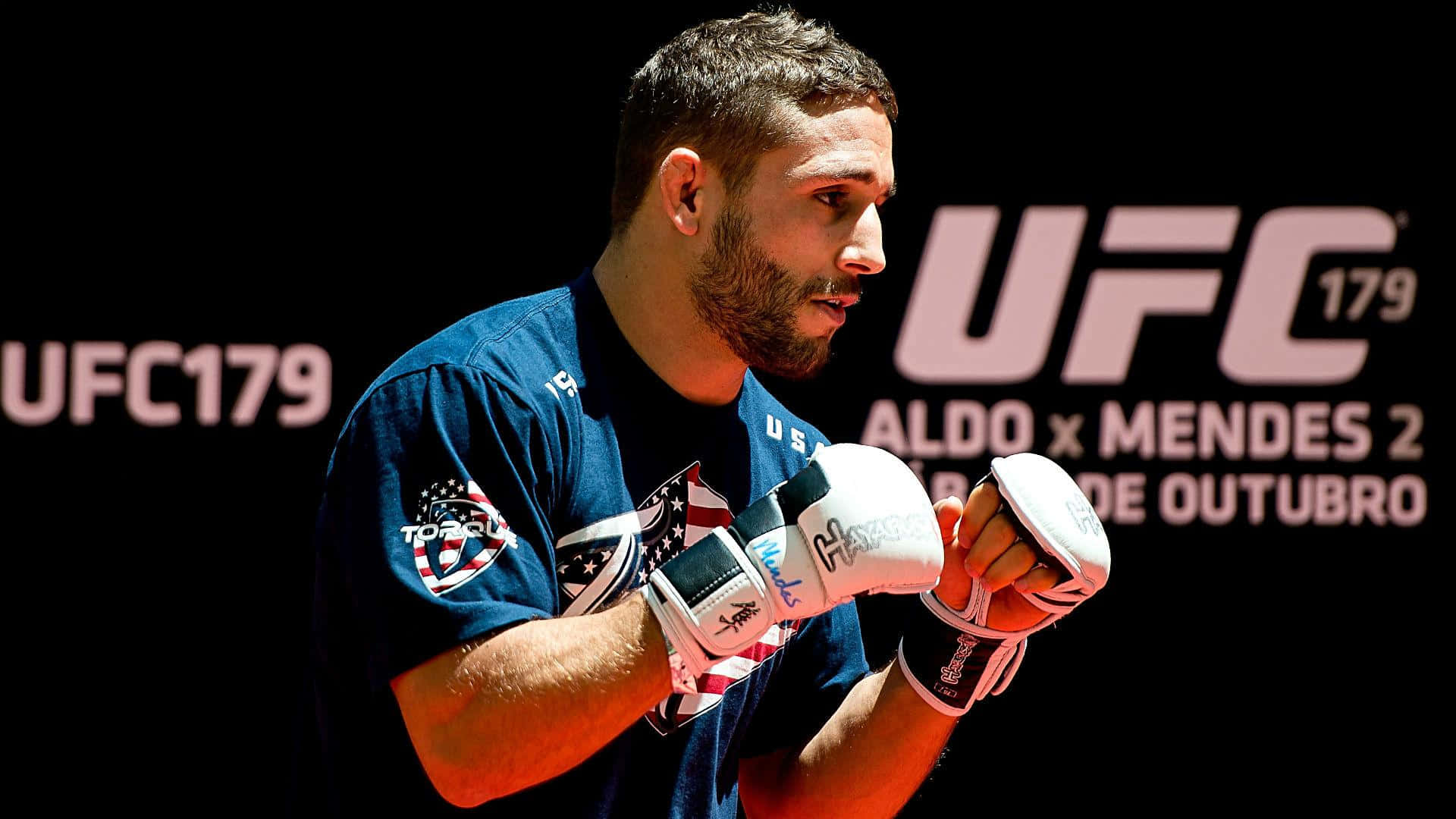 MMA 桌布 壁紙 — 一位專注的男性MMA拳擊手，戴著白色手套和藍色襯衫，在黑色UFC 179背景前準備就緒，背景上有活動文字。