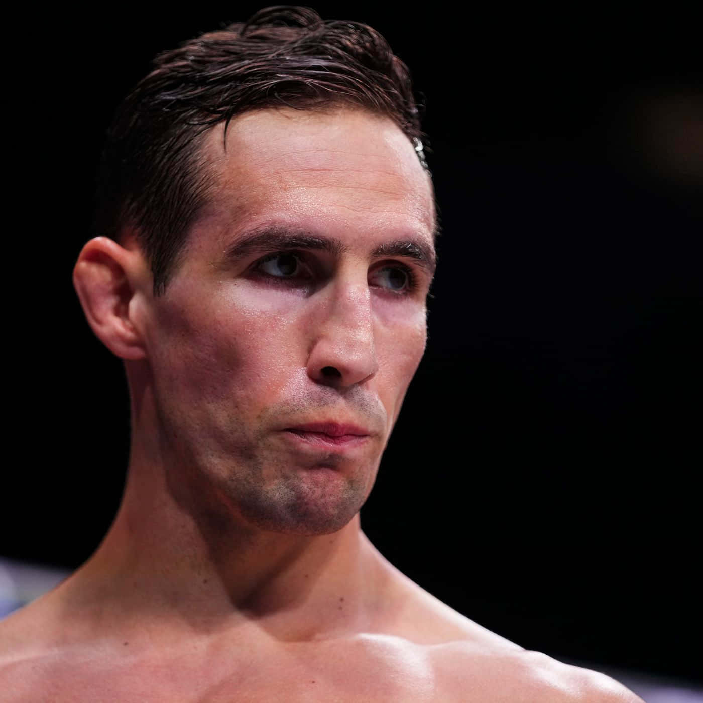 MMA 桌布 壁紙 — 一位專注的男性戰士，濕髮且眼神凌厲，在昏暗的競技場中凝視前方。