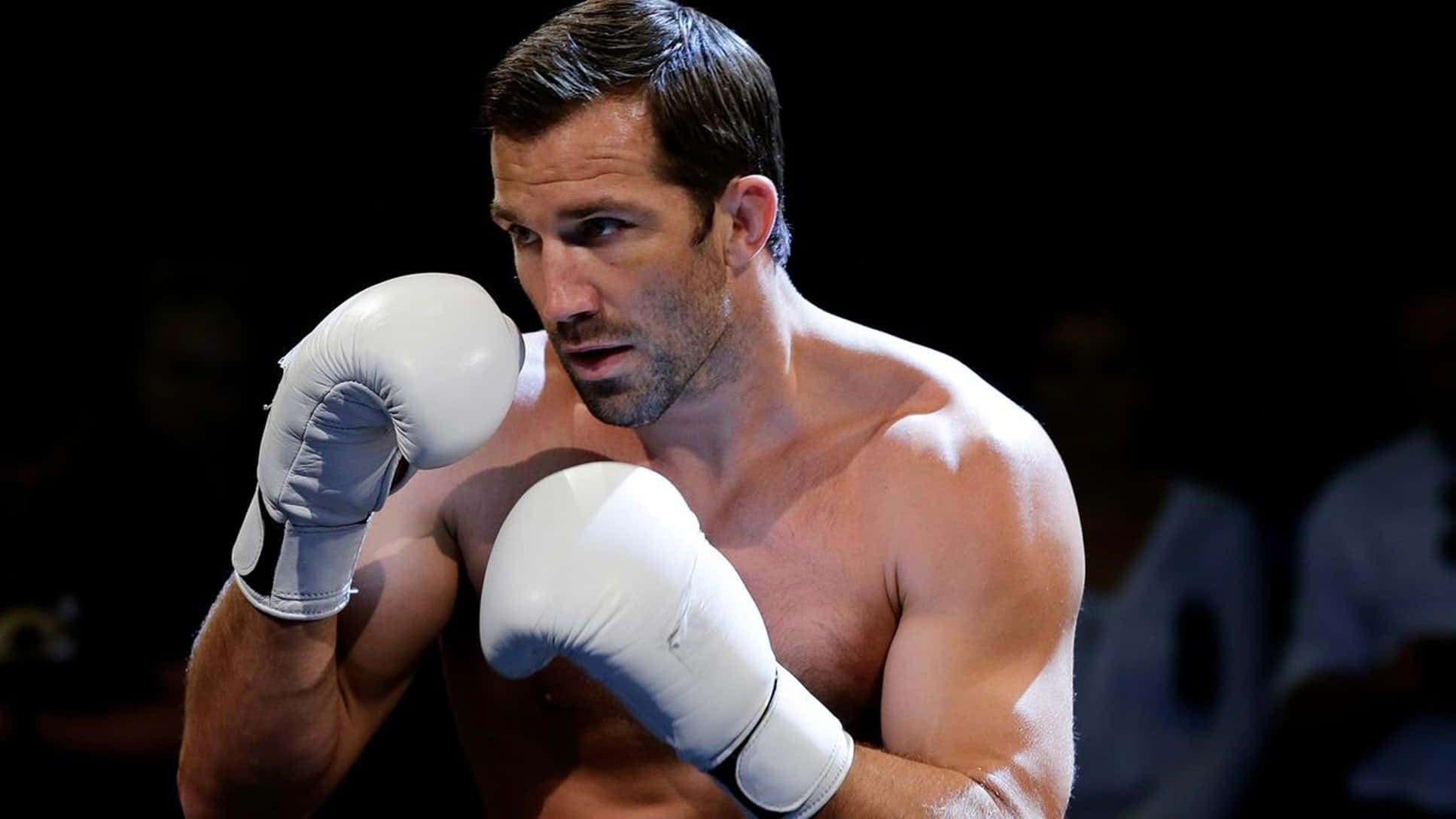 UFC 桌布 壁紙 — 一位專注的男性拳擊手戴著白色手套，在昏暗的擂台上以強烈的決心準備就緒。