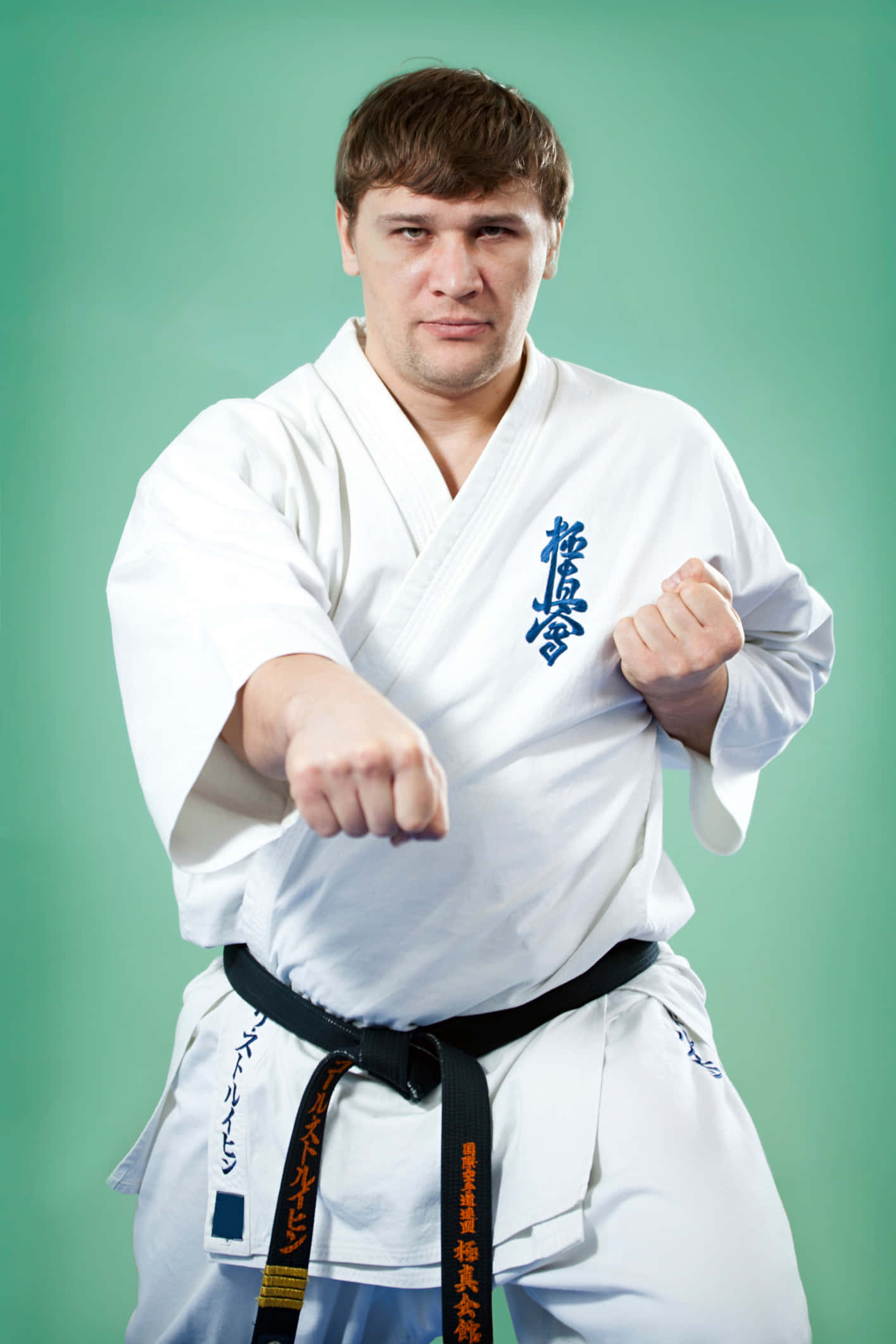 Taekwondo Uniform 桌布 壁紙 — 一位專注的男性武術家，身穿白色道服和黑色腰帶，在純綠色攝影棚背景前向前出擊。
