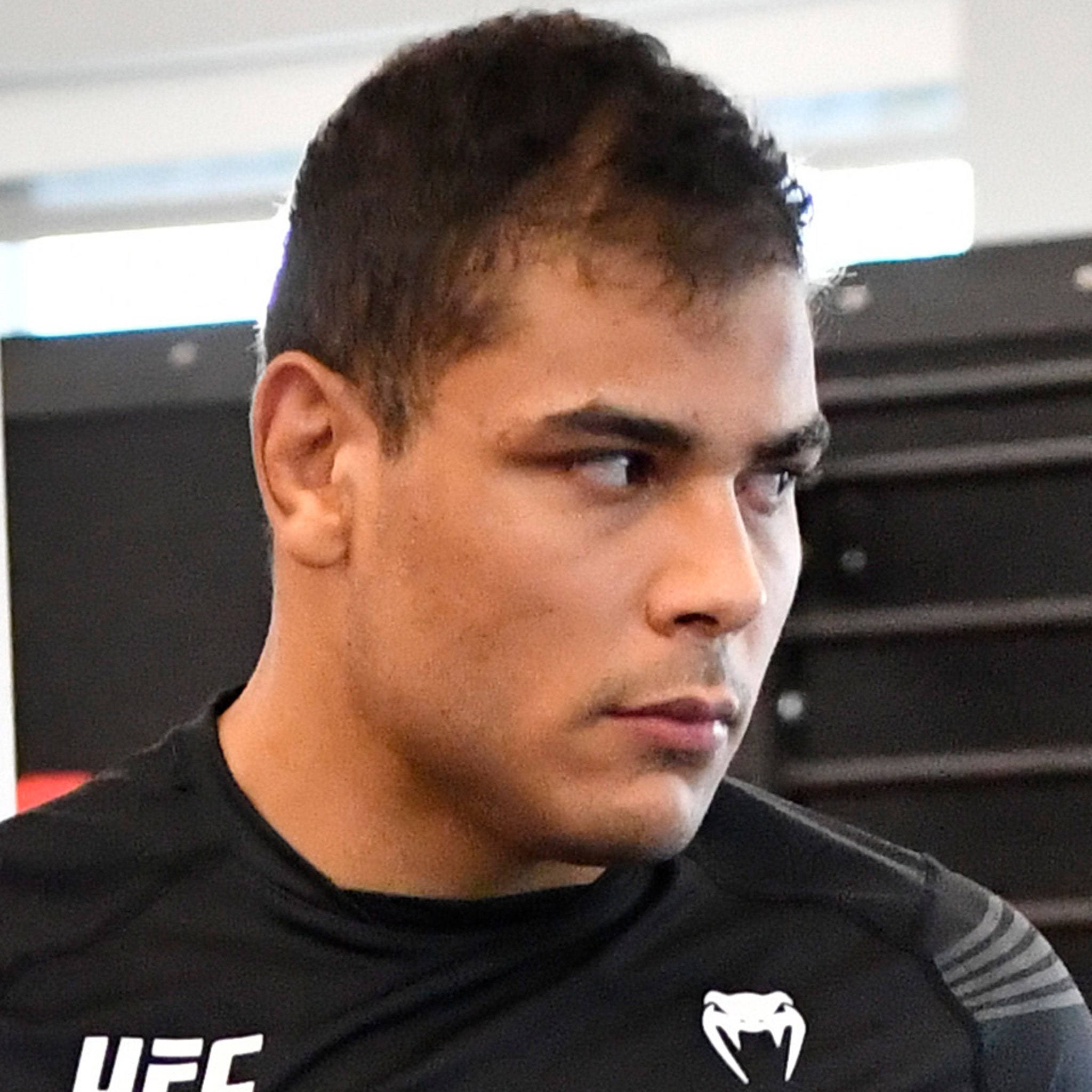 UFC 桌布 壁紙 — 一位專注的男性混合武術家，身穿黑色UFC襯衫，在健身房環境中凝視鏡頭外。