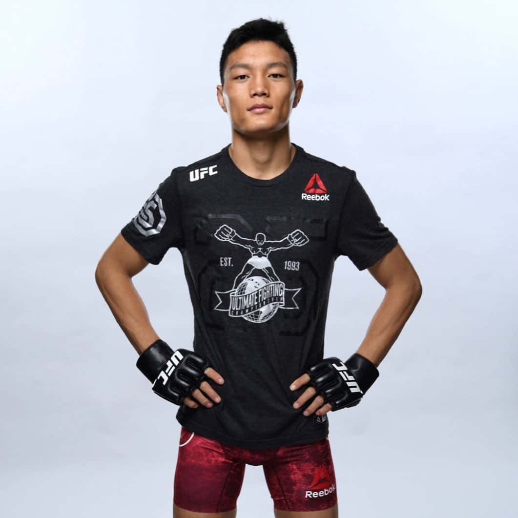 UFC 桌布 壁紙 — 一位專注的男性綜合格鬥選手身穿UFC裝備，雙手叉腰，自信地站在簡約的攝影棚背景前。