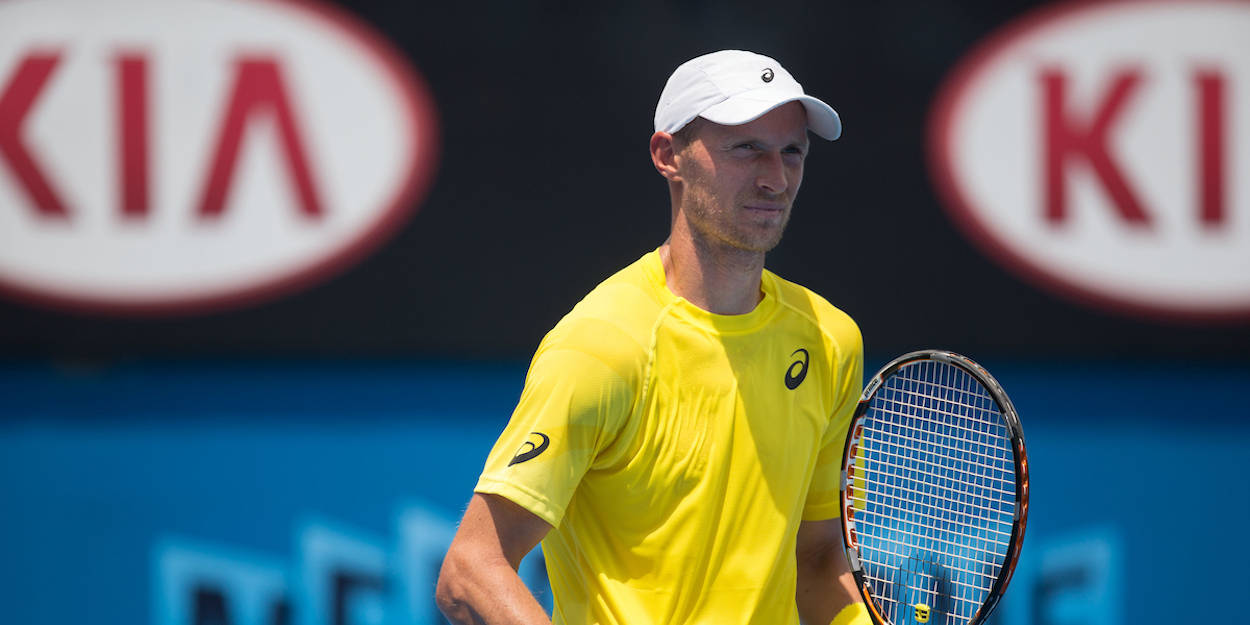 Tennis 桌布 壁紙 — 一位專注的男性網球運動員，身穿亮黃色襯衫和白色帽子，在藍色球場上握著球拍，背景有模糊的Kia標誌。