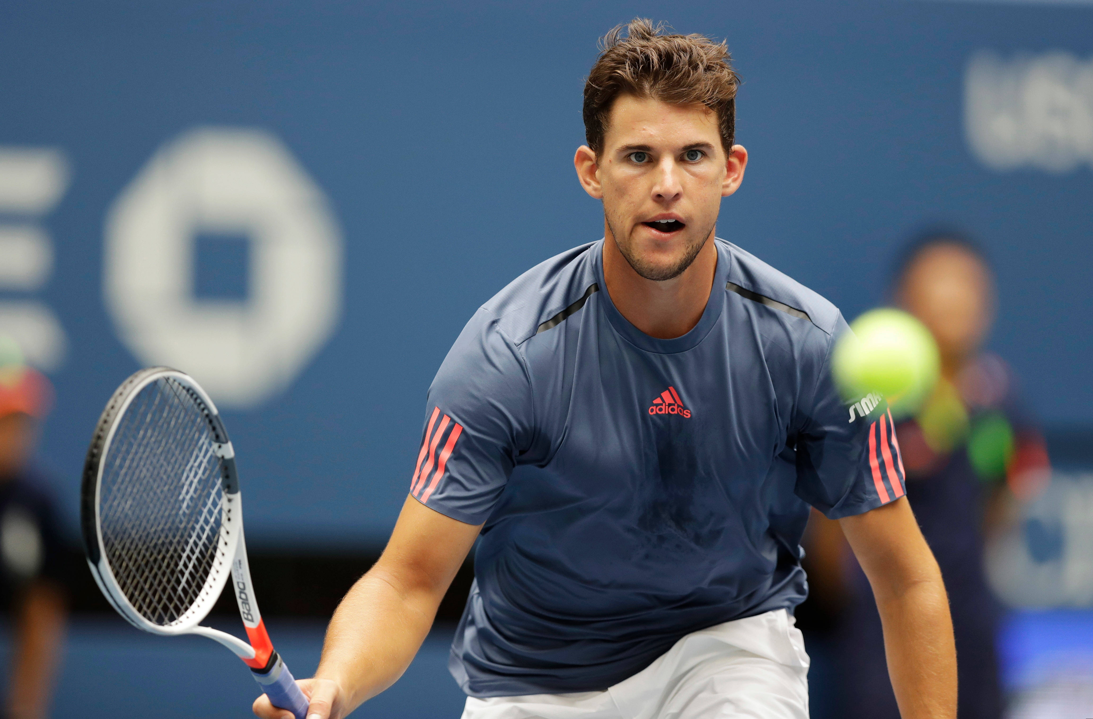 dominic thiem 桌布 壁紙 — 一位專注的男性網球運動員在揮拍中途，用球拍擊打一個亮黃色的球，背景是藍色球場。