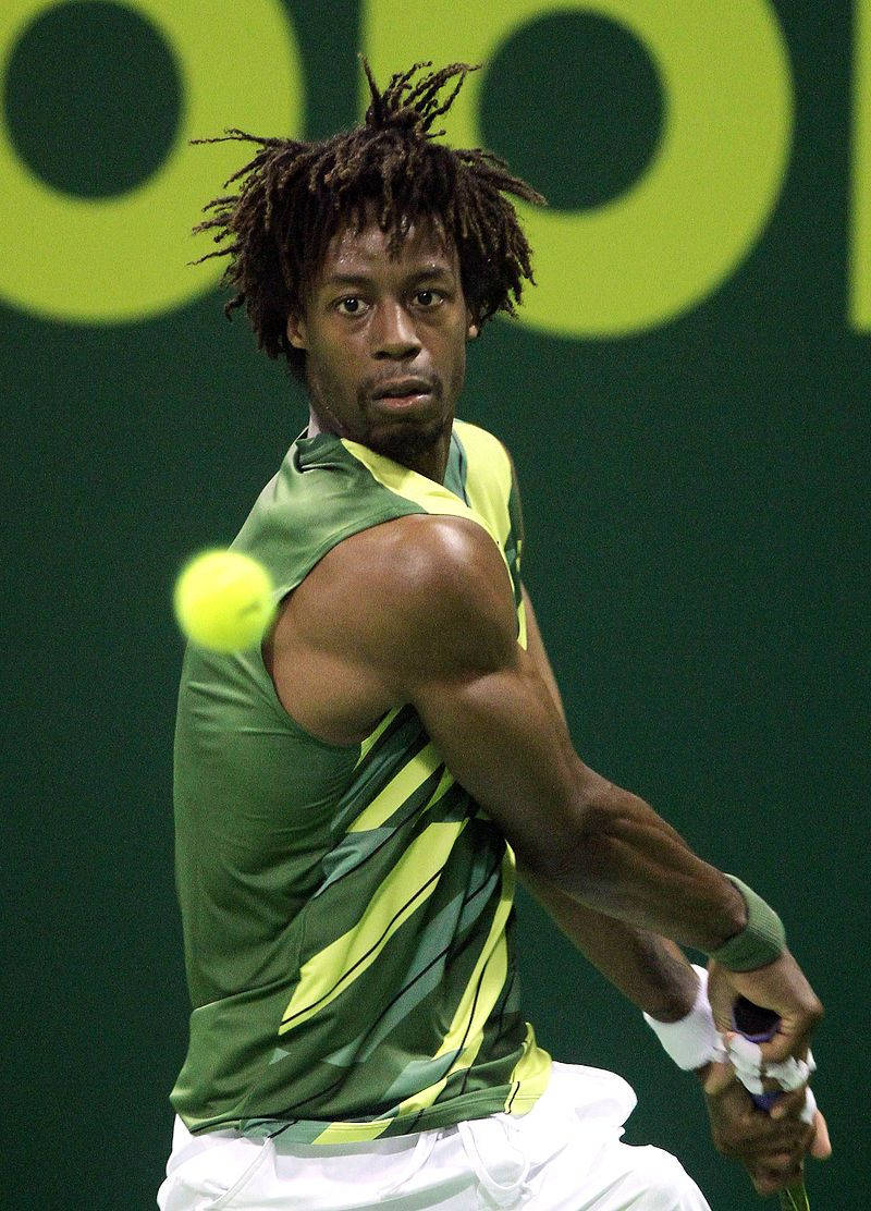 Tennis 桌布 壁紙 — 一位專注的男性網球運動員留著辮子，在綠色牆壁背景下揮拍擊打一個亮黃色的球。