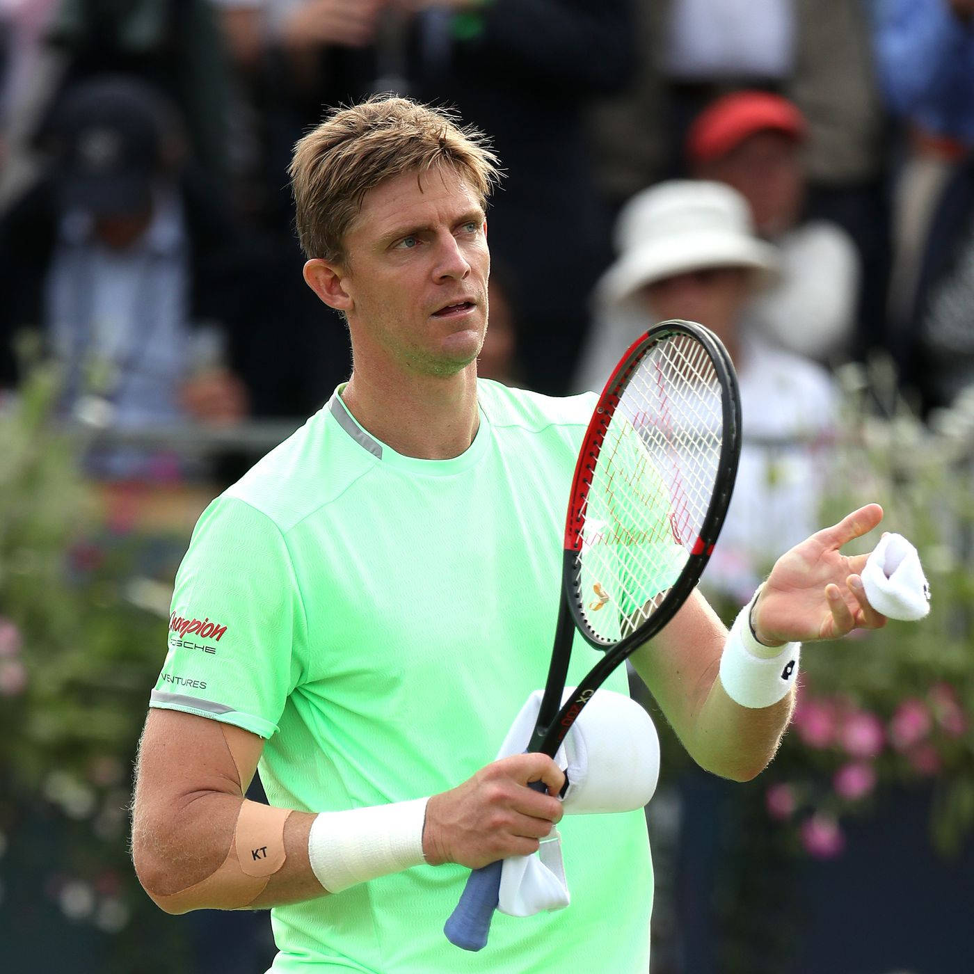 Tennis 桌布 壁紙 — 一位專注的男性網球運動員穿著亮綠色襯衫，在草地比賽中拿著球拍和毛巾。
