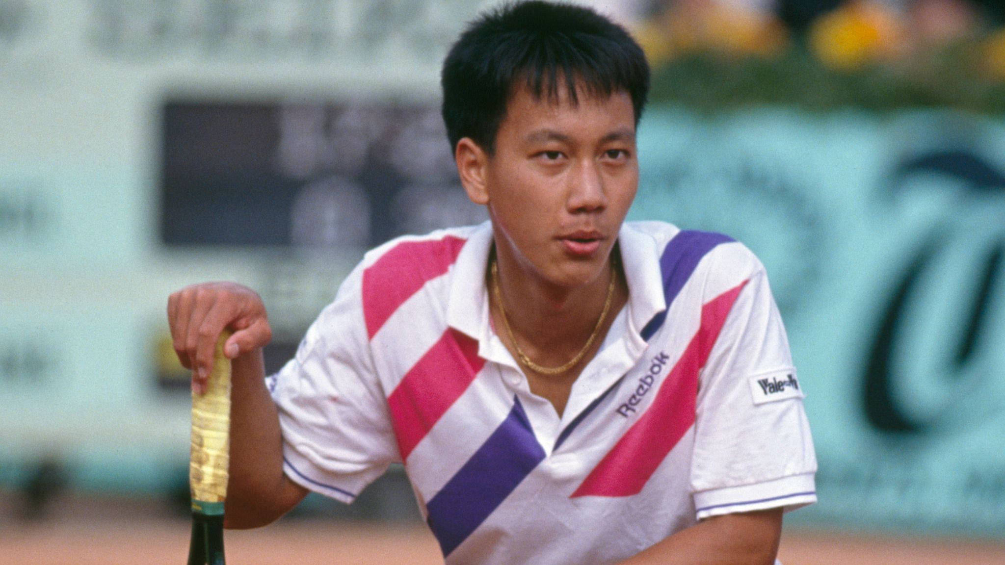 Tennis 桌布 壁紙 — 一位專注的男性網球運動員穿著條紋襯衫，在明亮的日光下於紅土球場握緊球拍。