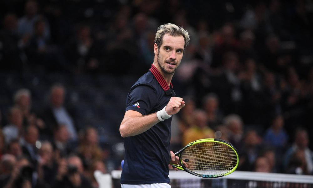 Tennis 桌布 壁紙 — 一位專注的男性網球運動員穿著深藍色襯衫，在比賽中握緊拳頭，手持黃色球拍，背景是模糊的人群。