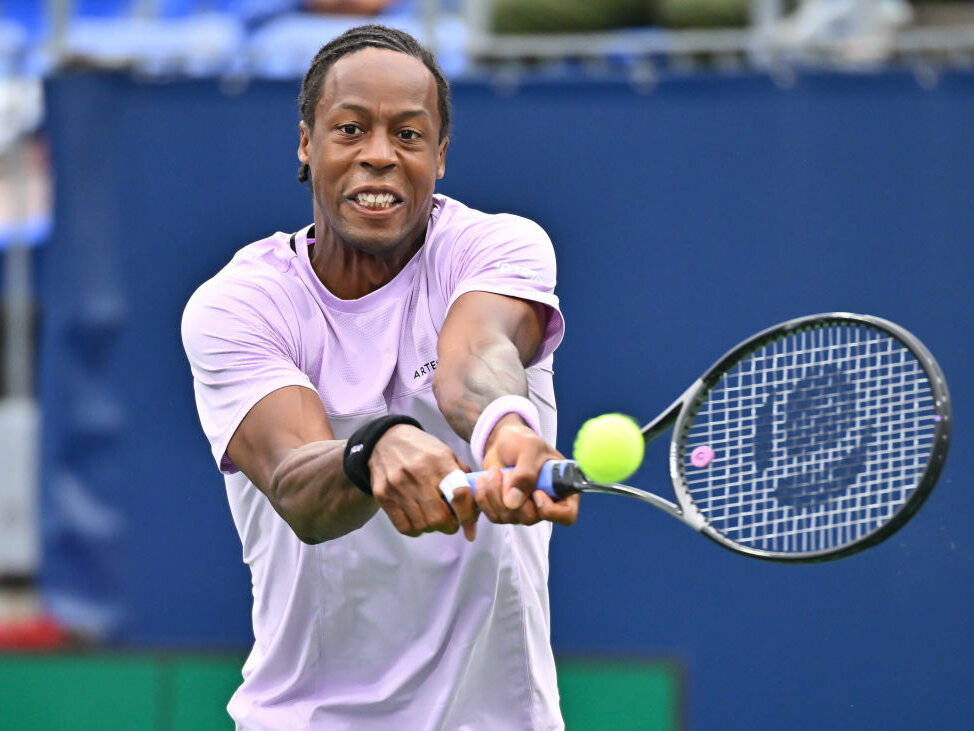 Tennis 桌布 壁紙 — 一位專注的男性網球運動員穿著淺紫色襯衫，在比賽中揮動球拍擊打明亮的黃色網球。