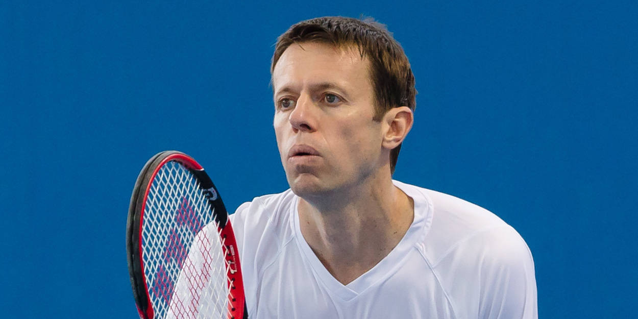Tennis 桌布 壁紙 — 一位專注的男性網球運動員穿著白色襯衫，在純藍色背景前拿著紅黑相間的球拍。