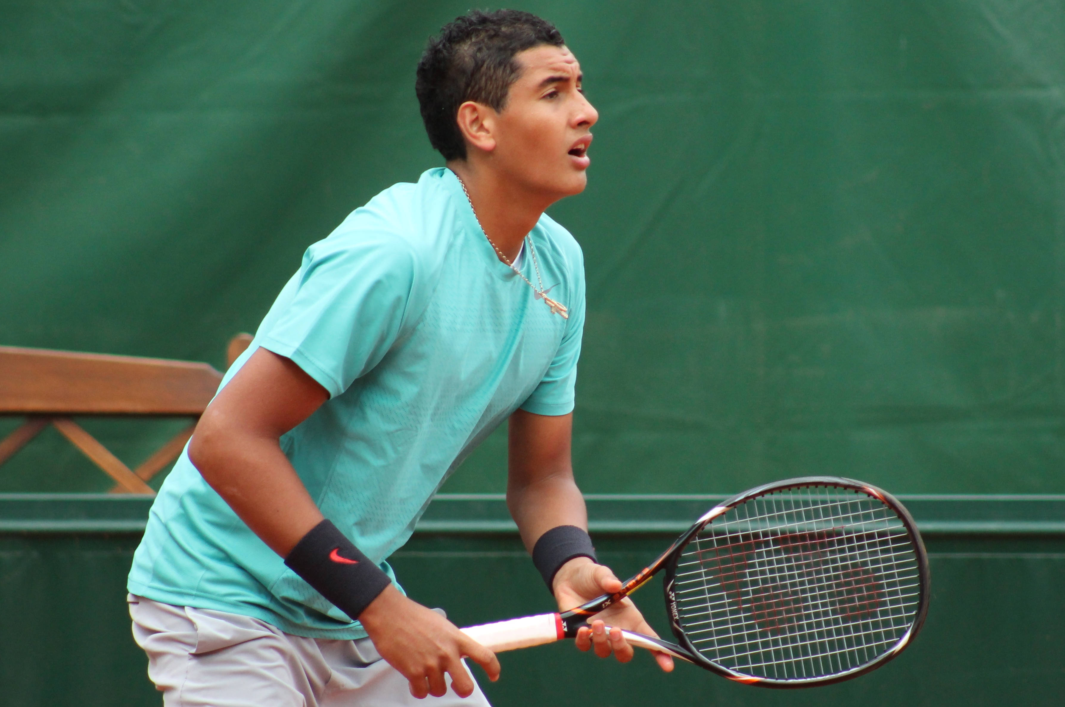 Kyrgios 桌布 壁紙 — 一位專注的男性網球運動員穿著青綠色襯衫，準備在綠色球場上用球拍擊球。