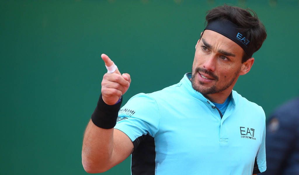 Tennis 桌布 壁紙 — 一位專注的男性網球運動員身穿淺藍色襯衫，在綠色球場背景下堅定地向前指。