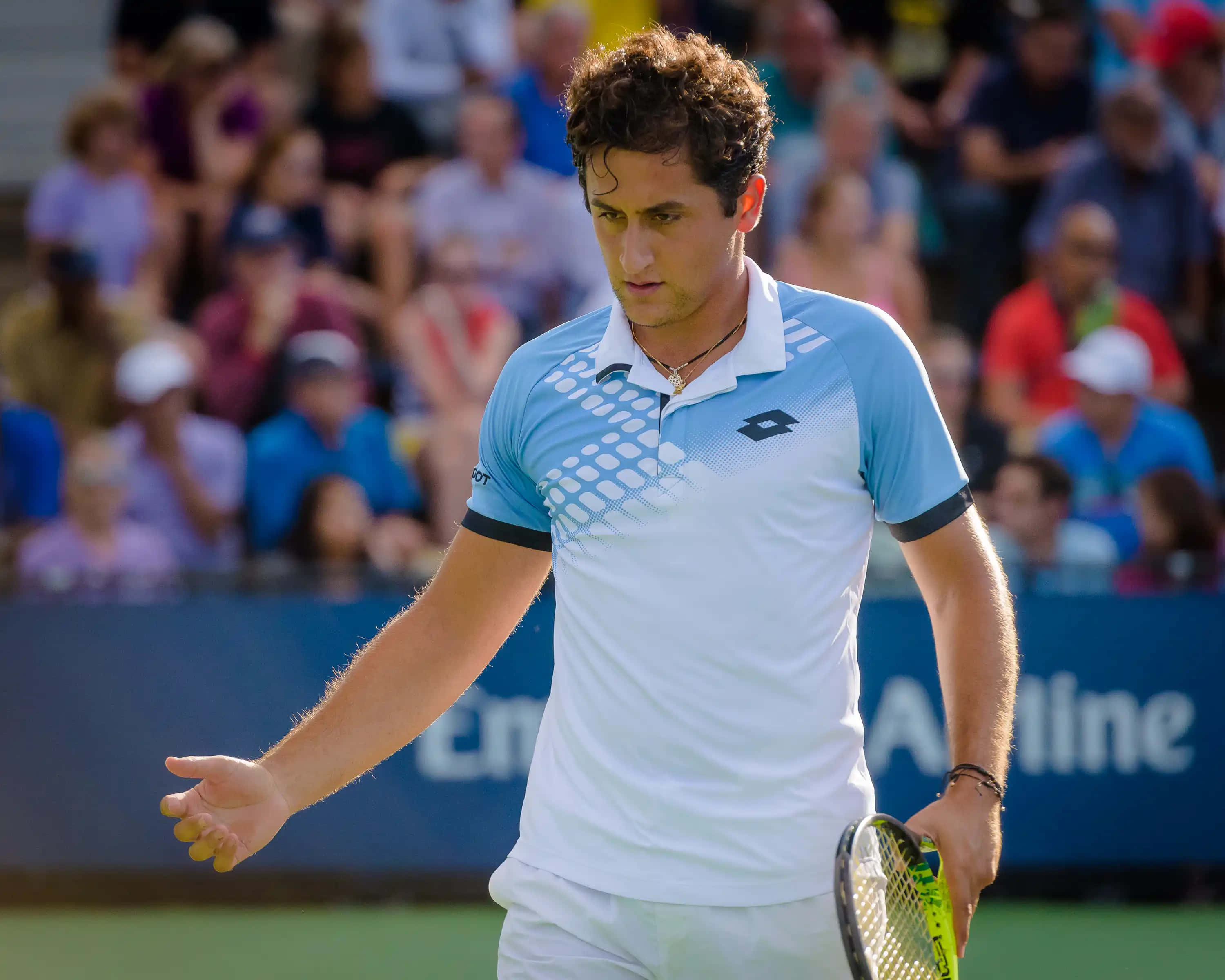 Tennis 桌布 壁紙 — 一位專注的男性網球運動員身穿淺藍色和白色襯衫，在綠色球場上握著球拍做手勢，背景有觀眾。