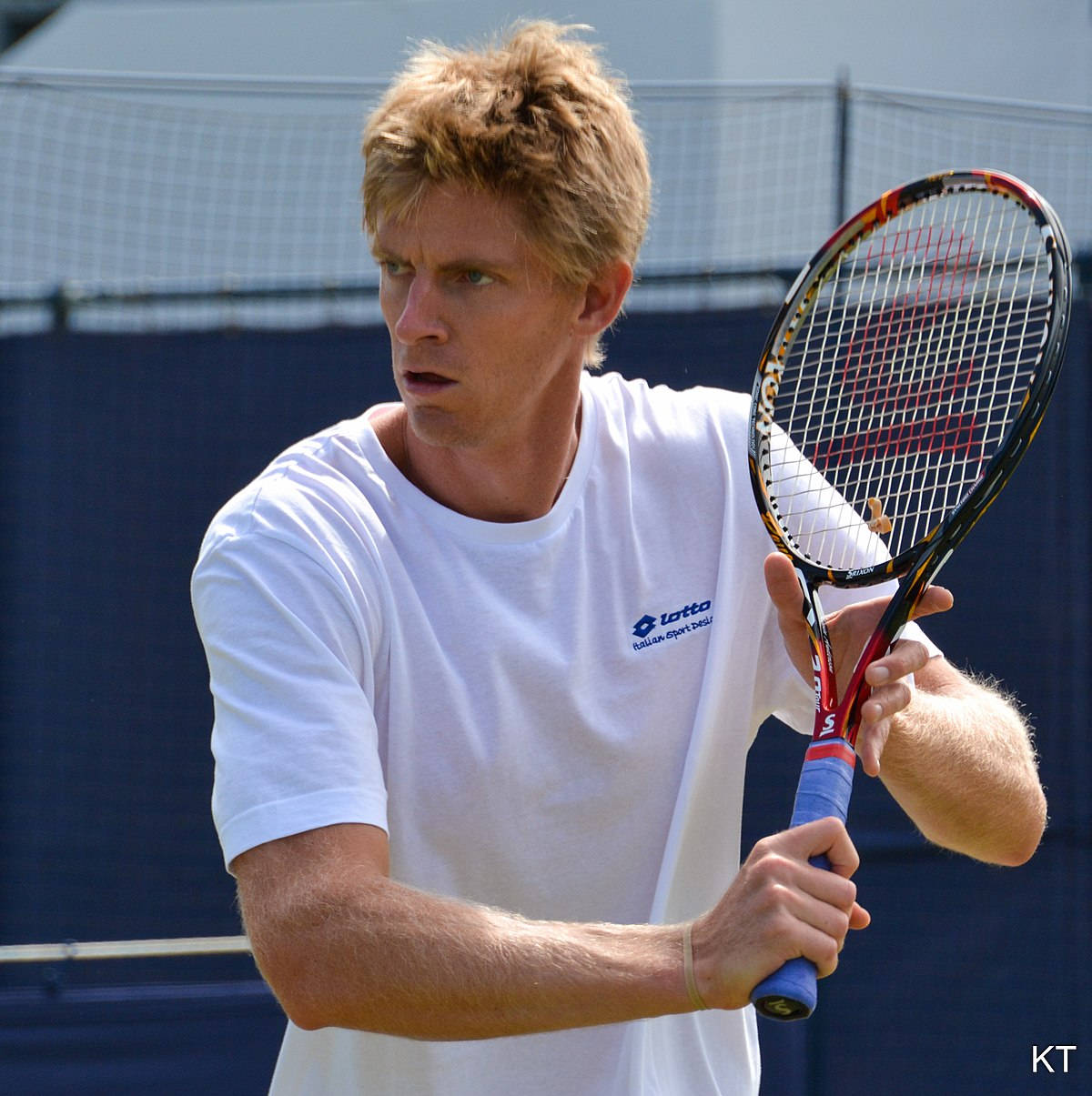 Tennis 桌布 壁紙 — 一位專注的男性網球運動員身穿白色襯衫，在陽光明媚的戶外球場上比賽中握緊球拍。