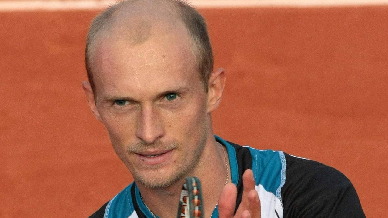 Tennis 桌布 壁紙 — 一位專注的男性網球選手，光頭藍眼，在紅土球場上握著球拍。