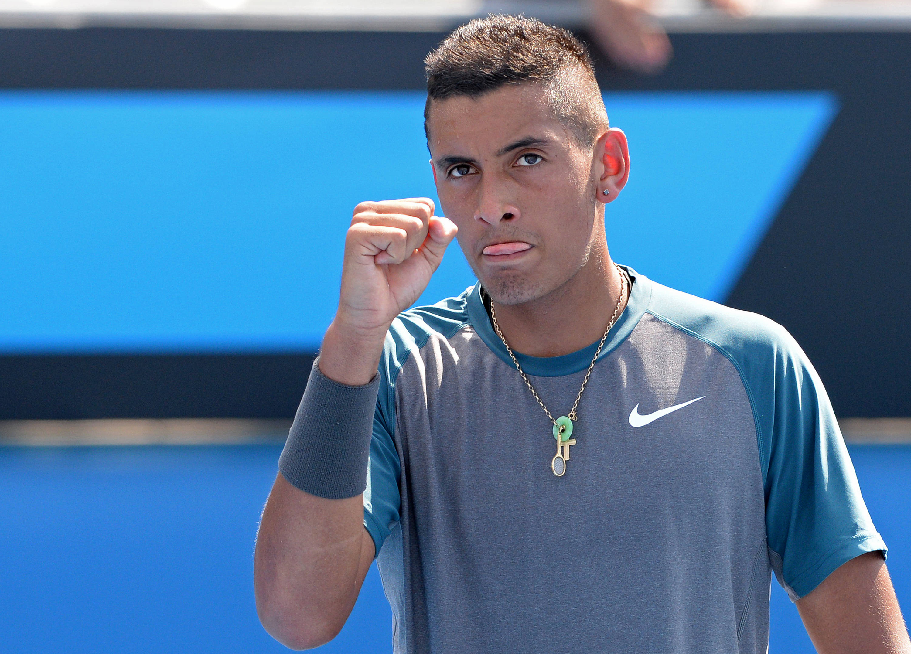 Kyrgios 桌布 壁紙 — 一位專注的男性網球選手，身穿灰色和藍色的Nike球衣，在充滿活力的藍色球場背景下握緊拳頭。