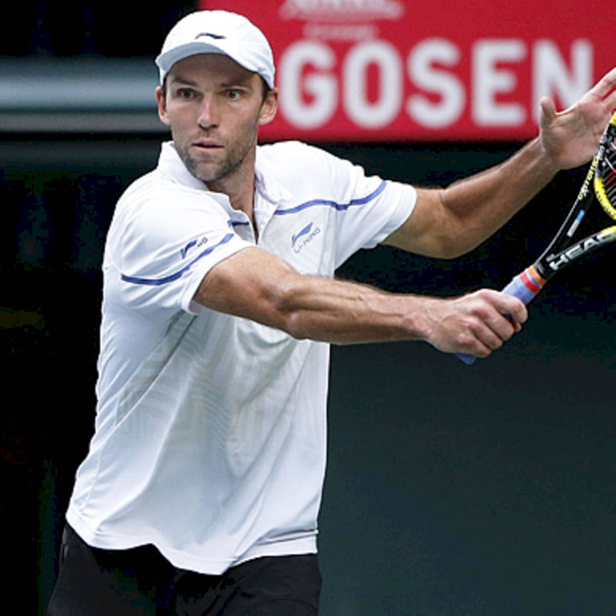 Tennis 桌布 壁紙 — 一位專注的男性網球選手，身穿白色襯衫和帽子，在模糊的球場背景下揮拍比賽。