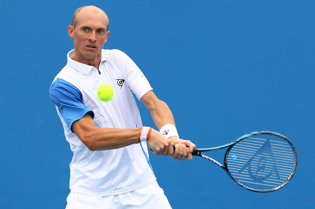 Tennis 桌布 壁紙 — 一位專注的男性網球選手，身穿白色和藍色裝備，在純藍色背景上揮拍擊打明亮的黃色網球。