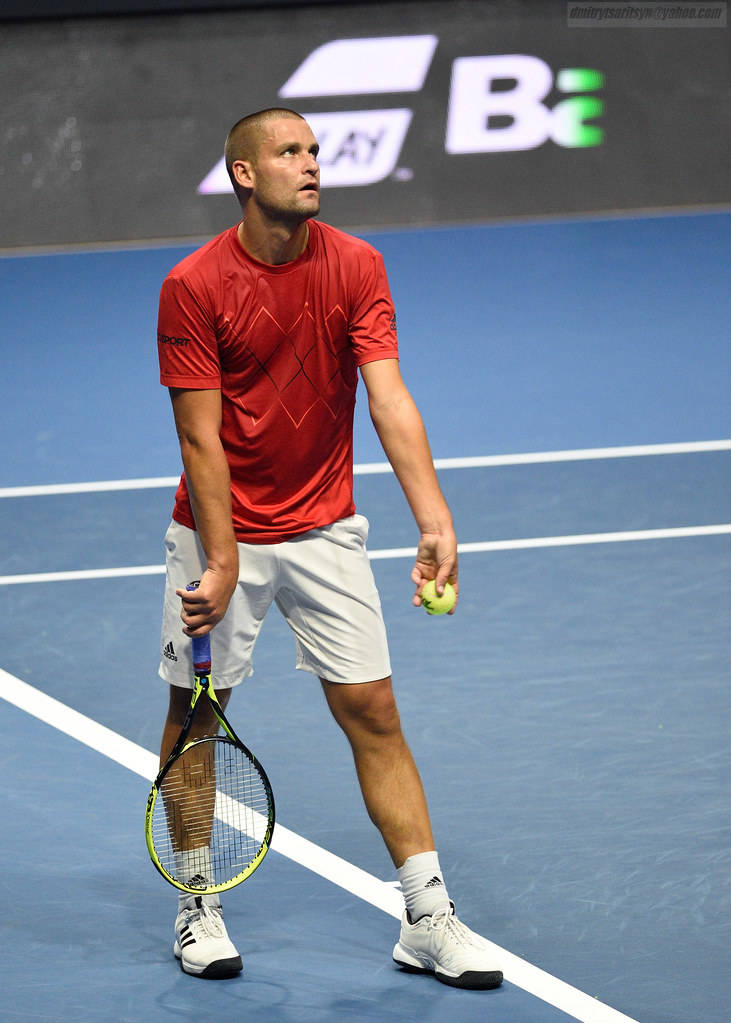 Tennis 桌布 壁紙 — 一位專注的男性網球選手，身穿紅色襯衫和白色短褲，在藍色硬地球場上準備好，手持球拍和球。