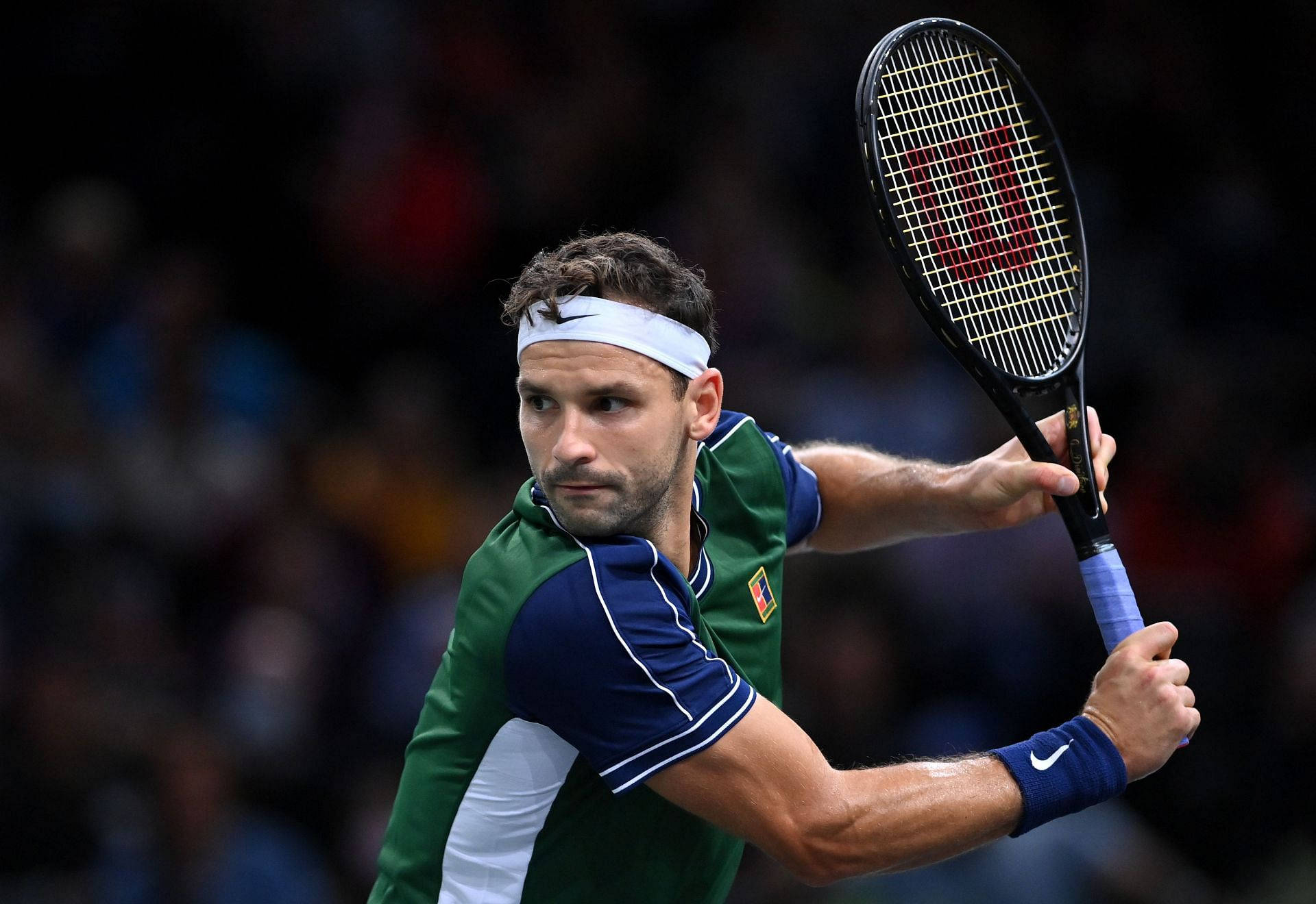 Tennis 桌布 壁紙 — 一位專注的男性網球選手，身穿綠色和藍色裝備，在明亮的體育場燈光下進行激烈比賽時揮動球拍。