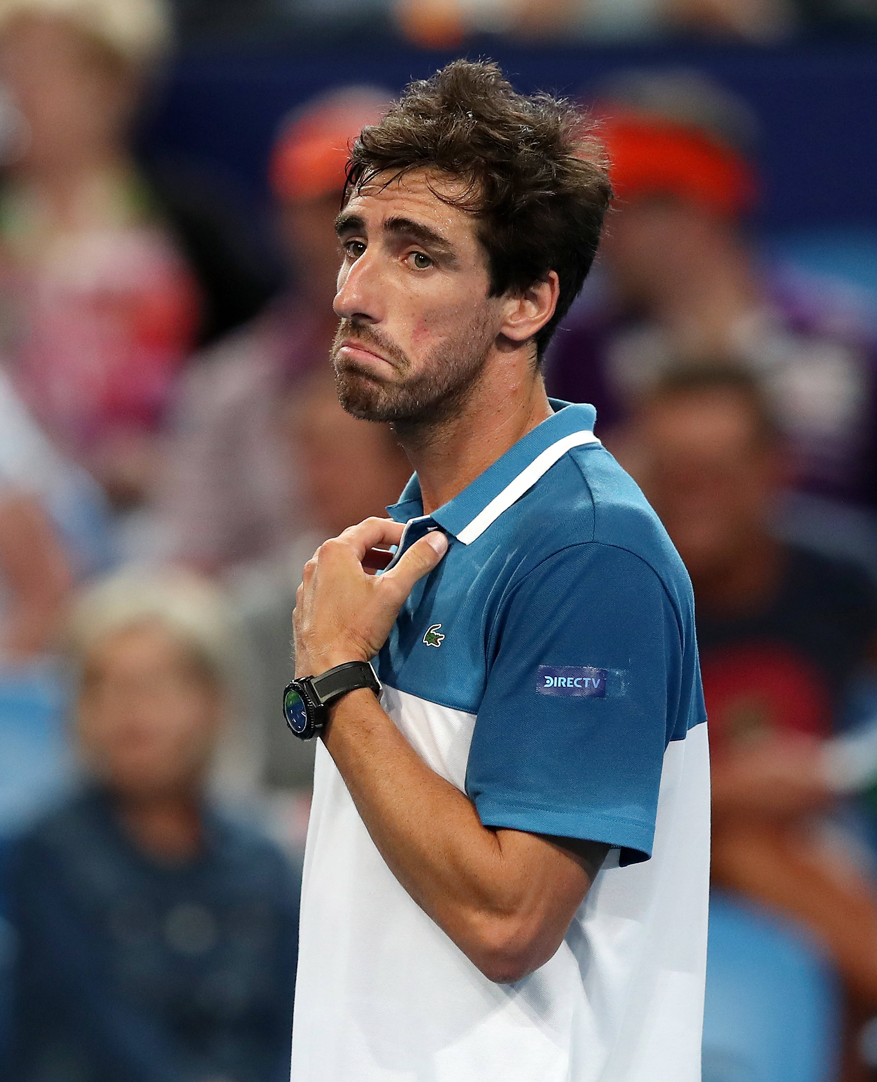 Tennis 桌布 壁紙 — 一位專注的男性網球選手，身穿藍白相間的Polo衫，在明亮的體育場燈光下比賽時調整衣領。