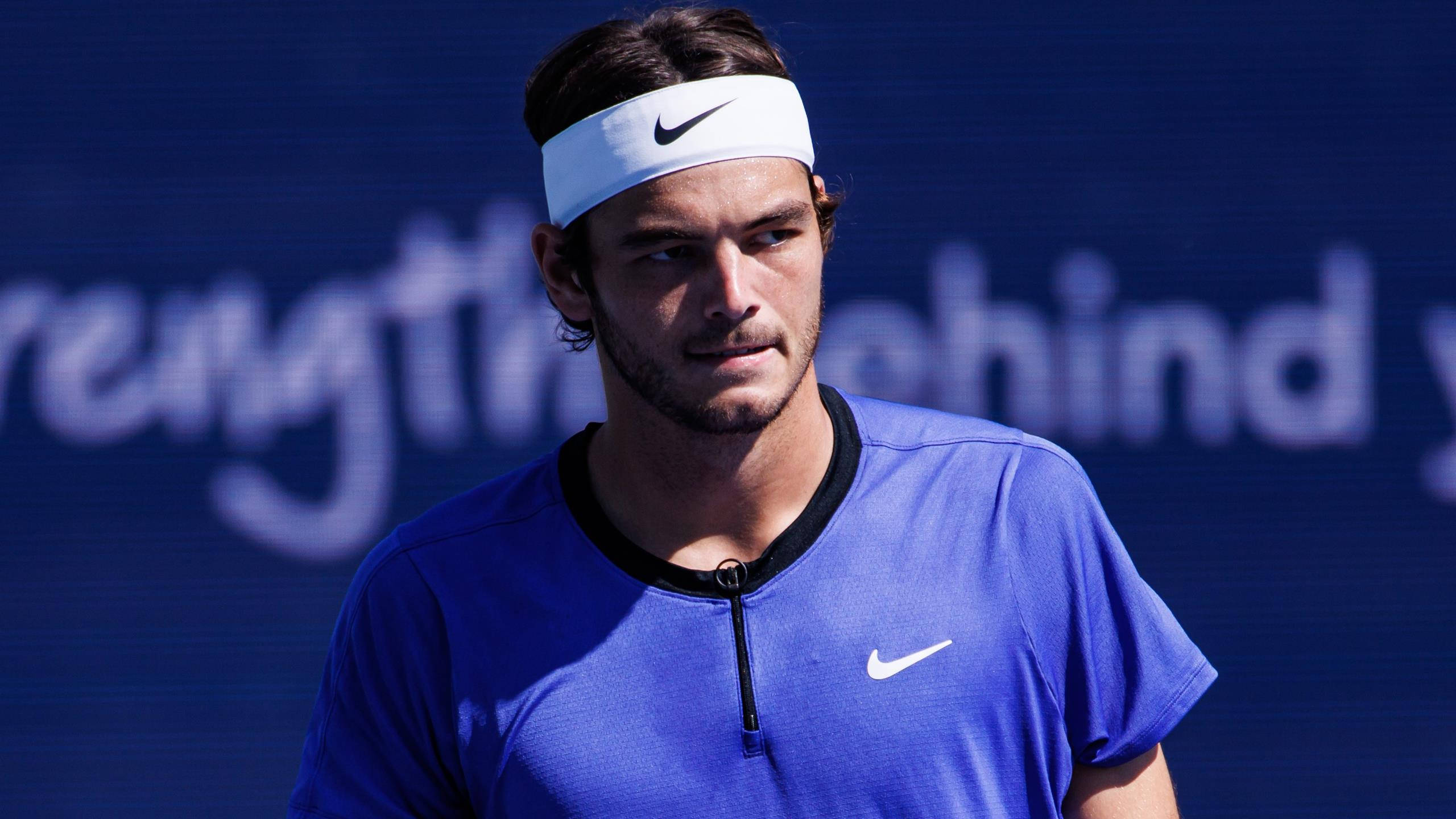 運動 桌布 壁紙 — 一位專注的男性網球選手，身穿藍色Nike襯衫和白色頭帶，站在球場上，背景是模糊的藍色。