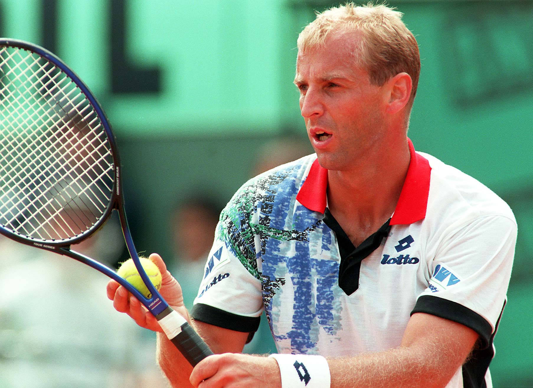 Tennis 桌布 壁紙 — 一位專注的男性網球選手在明亮的日光下，於紅土球場比賽中握著球拍和球。