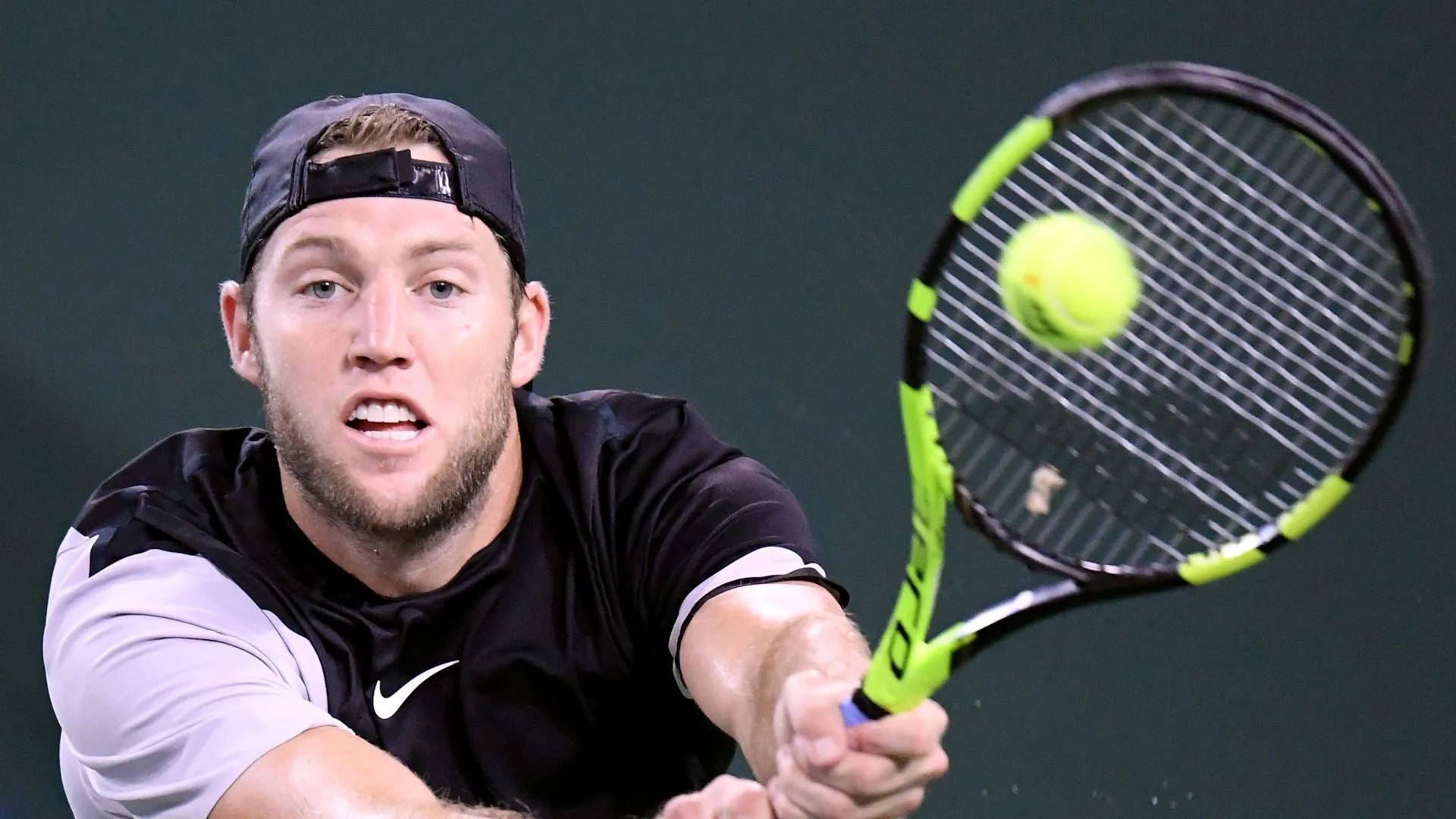 Tennis 桌布 壁紙 — 一位專注的男性網球選手在深綠色球場背景下揮動亮綠色球拍擊打黃色球。