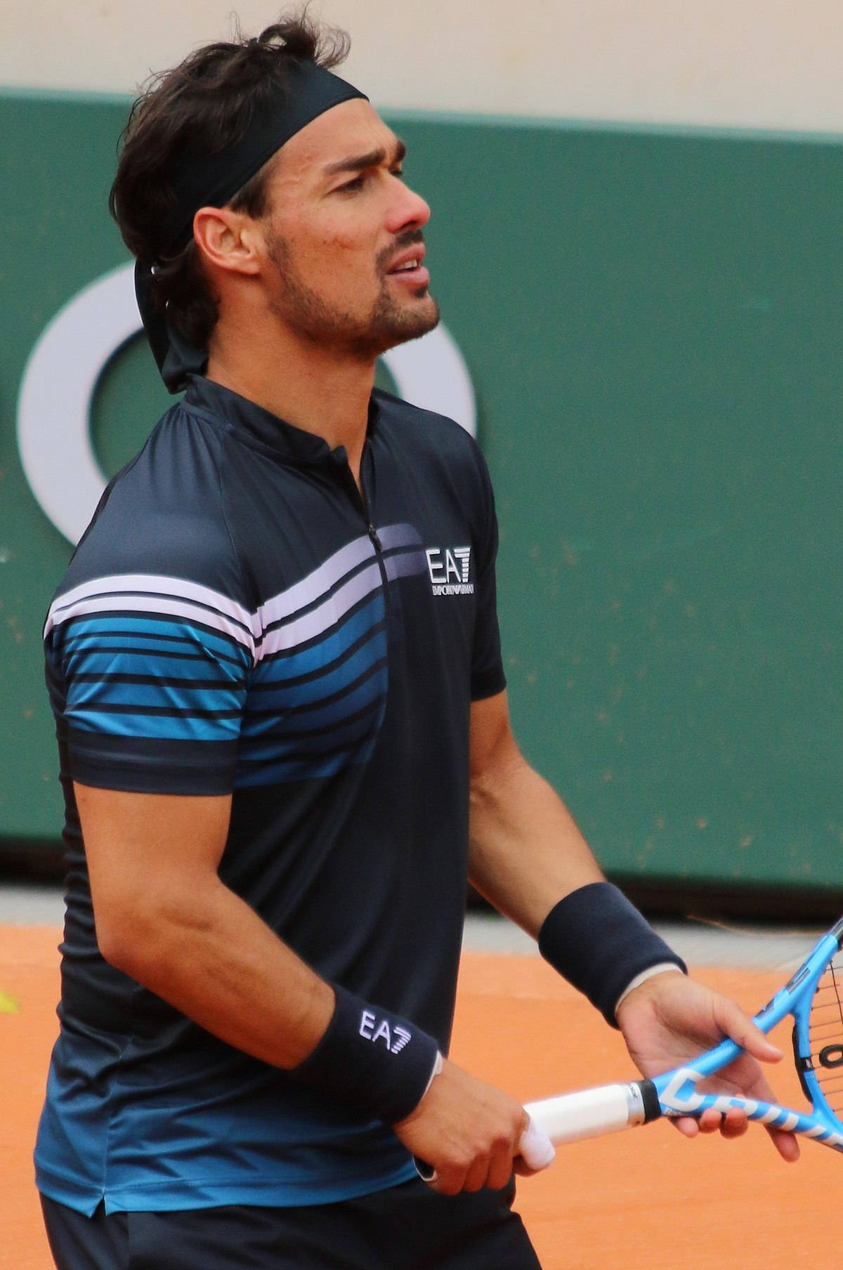 Tennis 桌布 壁紙 — 一位專注的男性網球選手在紅土球場上握著球拍，背景是綠色牆壁。