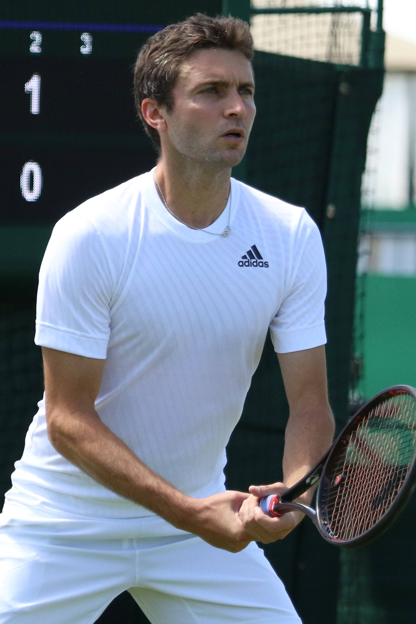 Athlete 桌布 壁紙 — 一位專注的男性網球選手穿著白色adidas裝備，在草地場上比賽中握著球拍，計分板清晰可見。