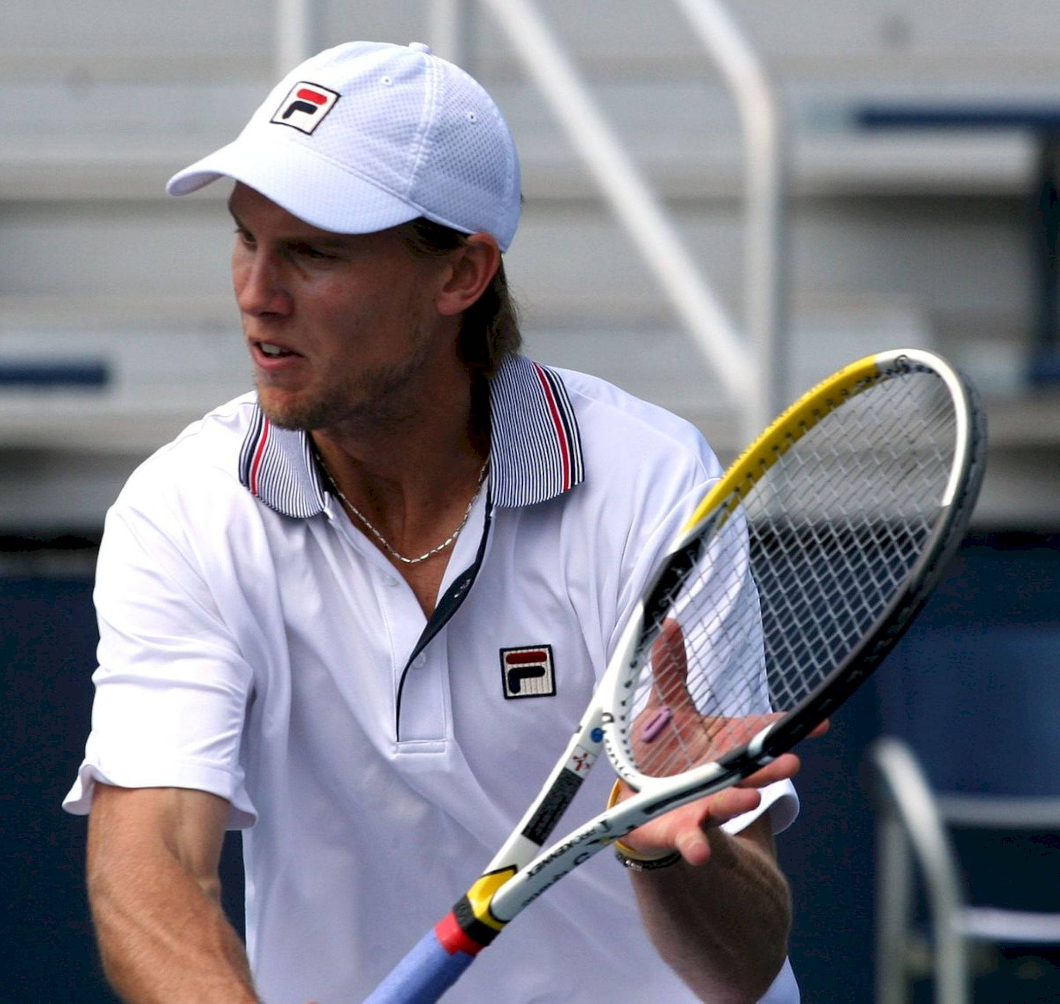Tennis 桌布 壁紙 — 一位專注的男性網球選手穿著白色裝備，在明亮的日光下於硬地球場比賽中握著球拍。