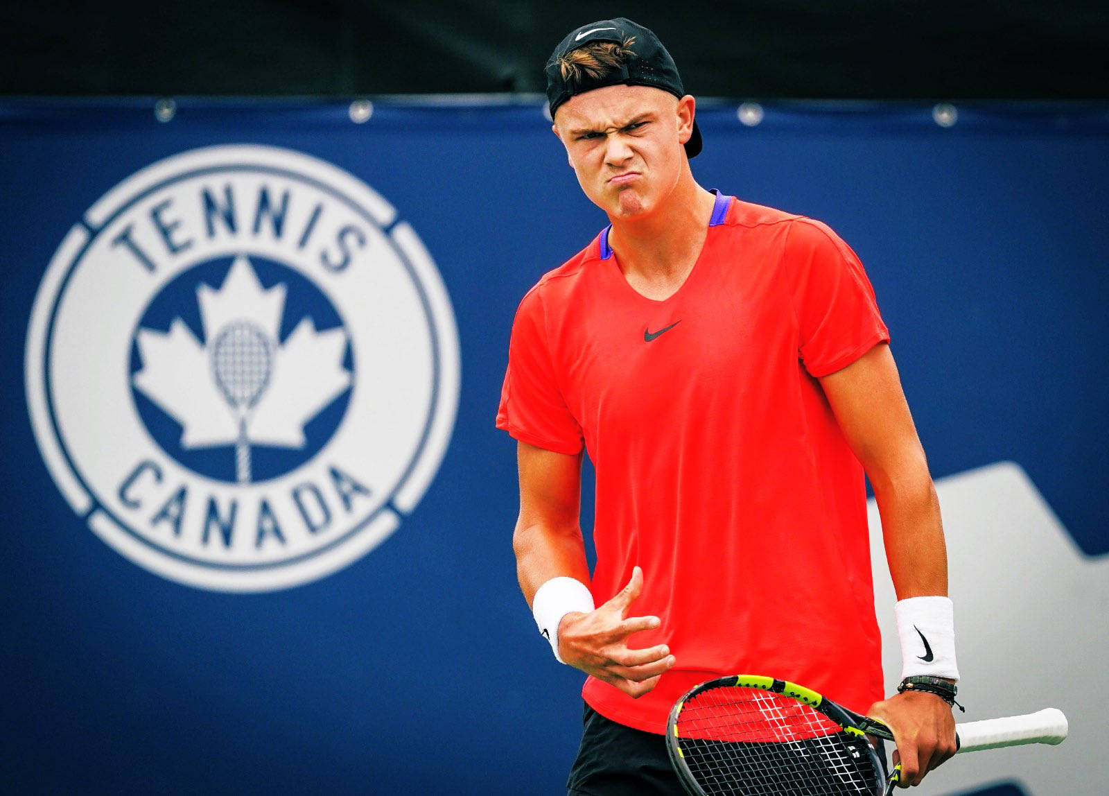 網球 桌布 壁紙 — 一位專注的男性網球選手穿著紅色襯衫，在藍色Tennis Canada背景前握著球拍，表情猙獰。