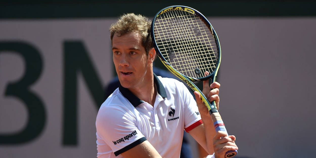 Tennis 桌布 壁紙 — 一位專注的男性網球選手身穿白色Polo衫，在陽光明媚的紅土球場上比賽中緊握球拍。
