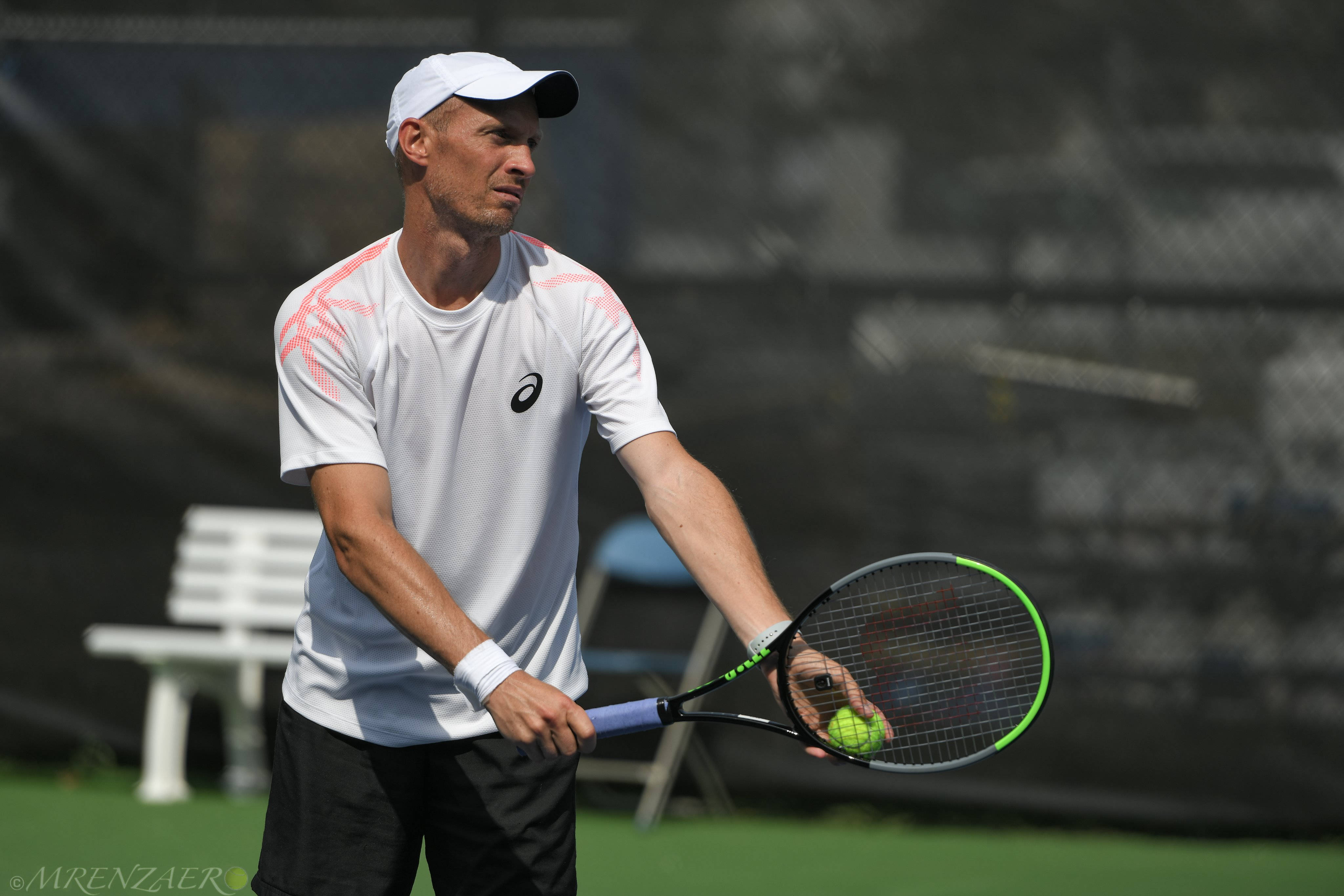 Tennis 桌布 壁紙 — 一位專注的男性網球選手身穿白色裝備，在陽光明媚的戶外球場上握著球拍和一顆亮綠色的球。