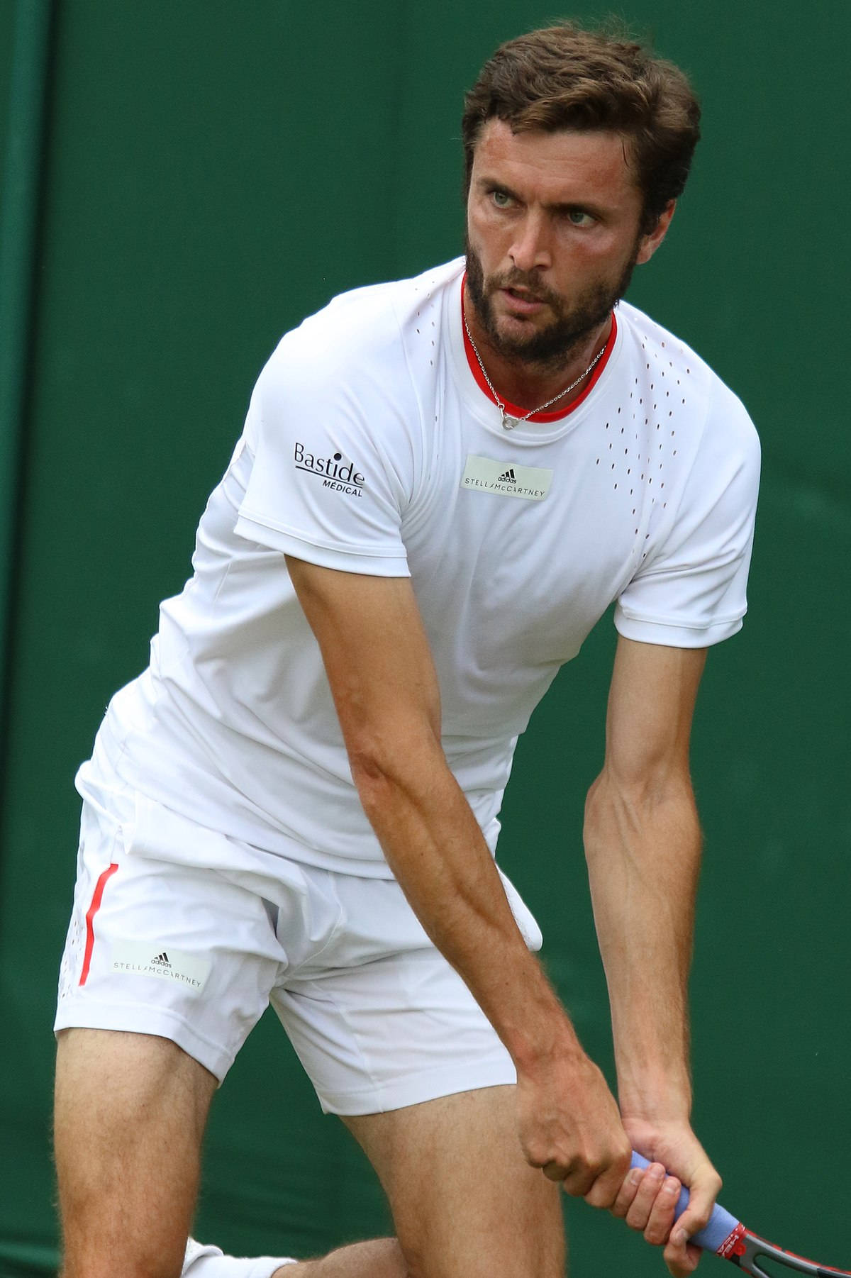Tennis 桌布 壁紙 — 一位專注的男性網球選手身穿白色裝備，在綠色背景下揮拍中途緊握球拍。