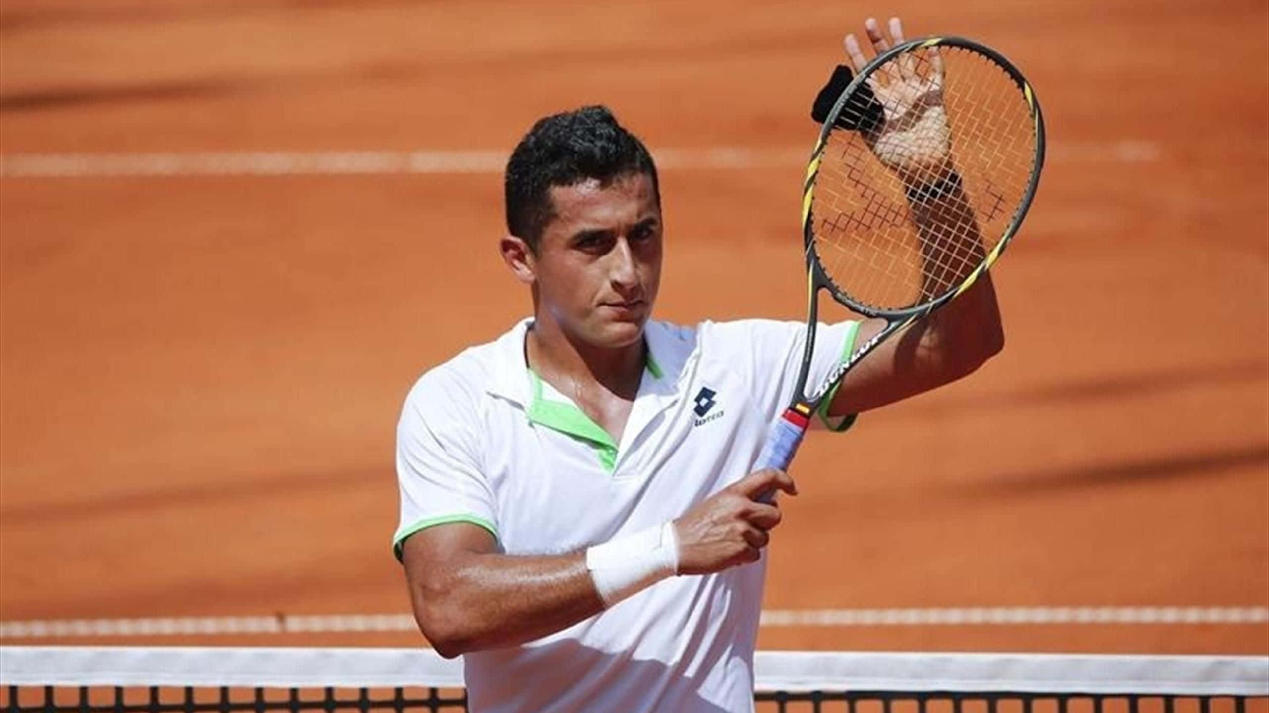 Tennis 桌布 壁紙 — 一位專注的男性網球選手身穿白色襯衫，在陽光普照的紅土球場上揮拍中。