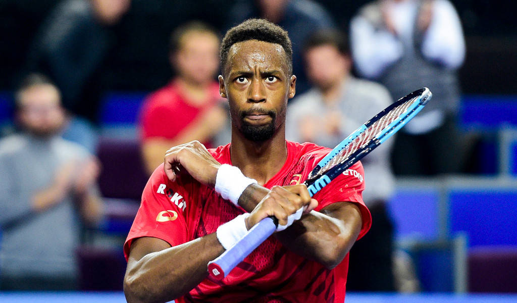 Tennis 桌布 壁紙 — 一位專注的男性網球選手身穿紅色上衣，在室內球場比賽中緊握球拍，身後有模糊的觀眾。