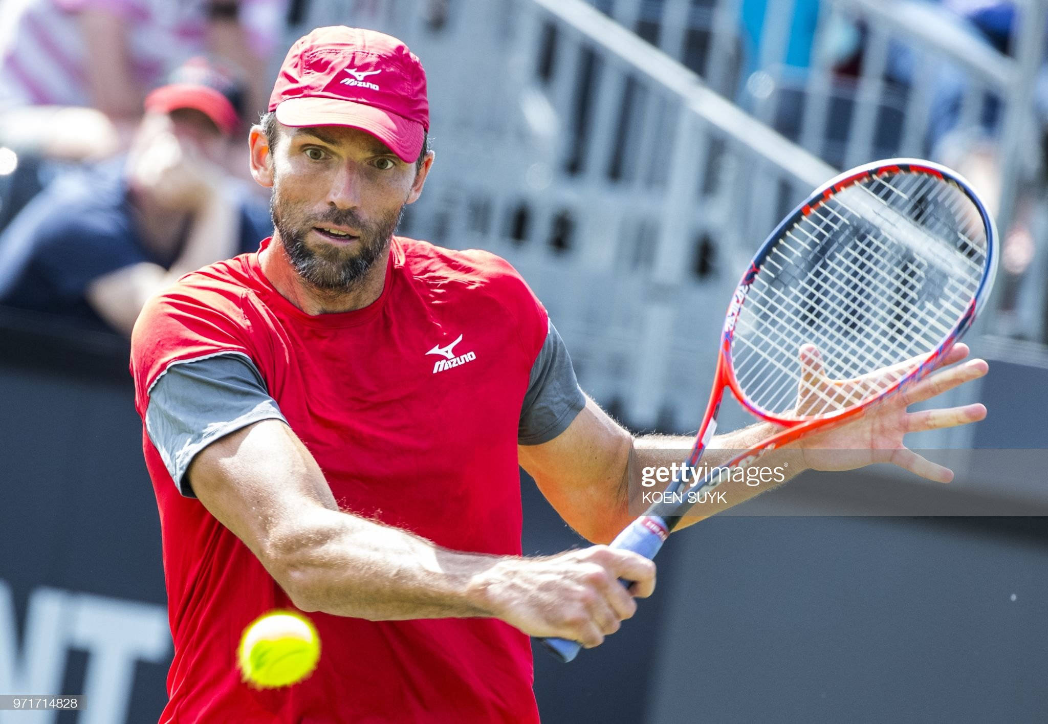 Athlete 桌布 壁紙 — 一位專注的男性網球選手身穿紅色裝備，在明亮的日間比賽中揮拍擊打黃色球。