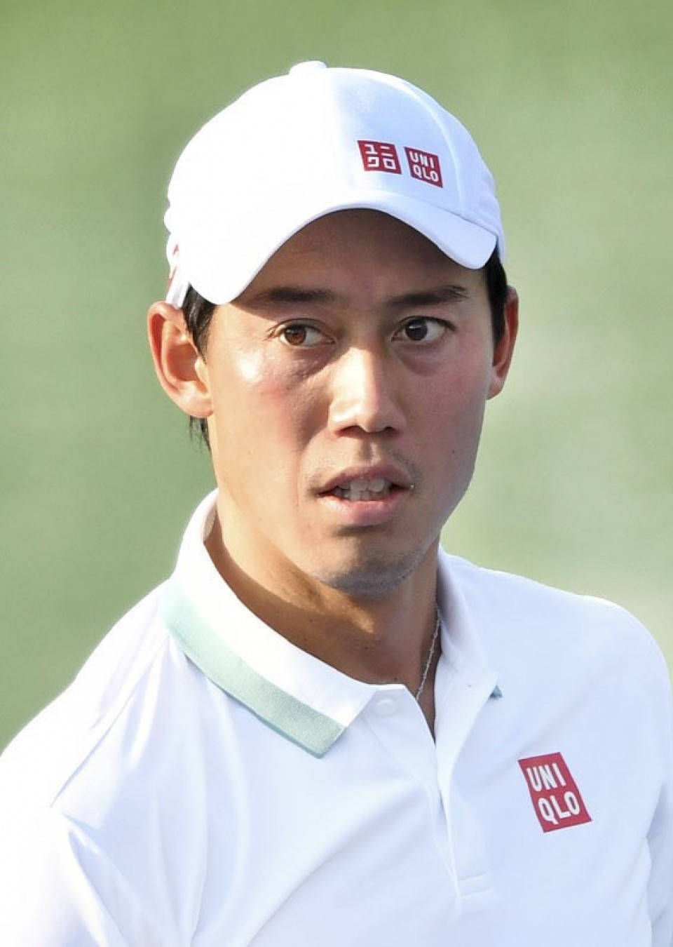 Athlete 桌布 壁紙 — 一位專注的男性高爾夫球手，戴著白色Uniqlo帽子和Polo衫，站在模糊的綠色背景前。