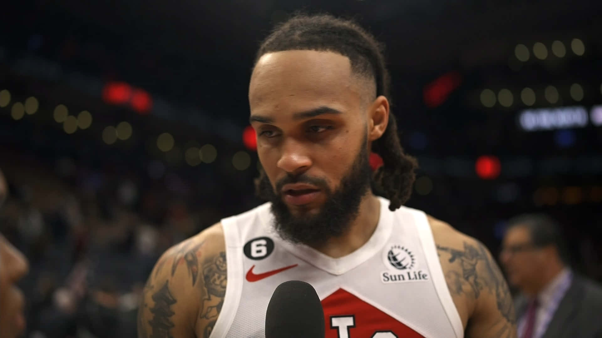 NBA 桌布 壁紙 — 一位專注的籃球運動員，留著辮子頭和刺青，在場館燈光下於賽後訪談中對著麥克風說話。