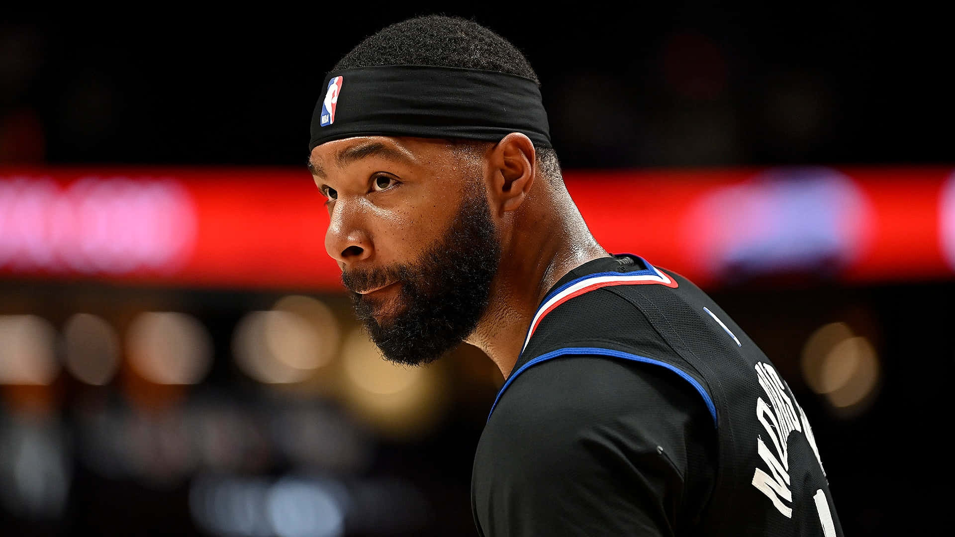 NBA 桌布 壁紙 — 一位專注的籃球運動員，留著鬍子並戴著頭帶，在明亮的場館燈光下於比賽中怒目凝視。