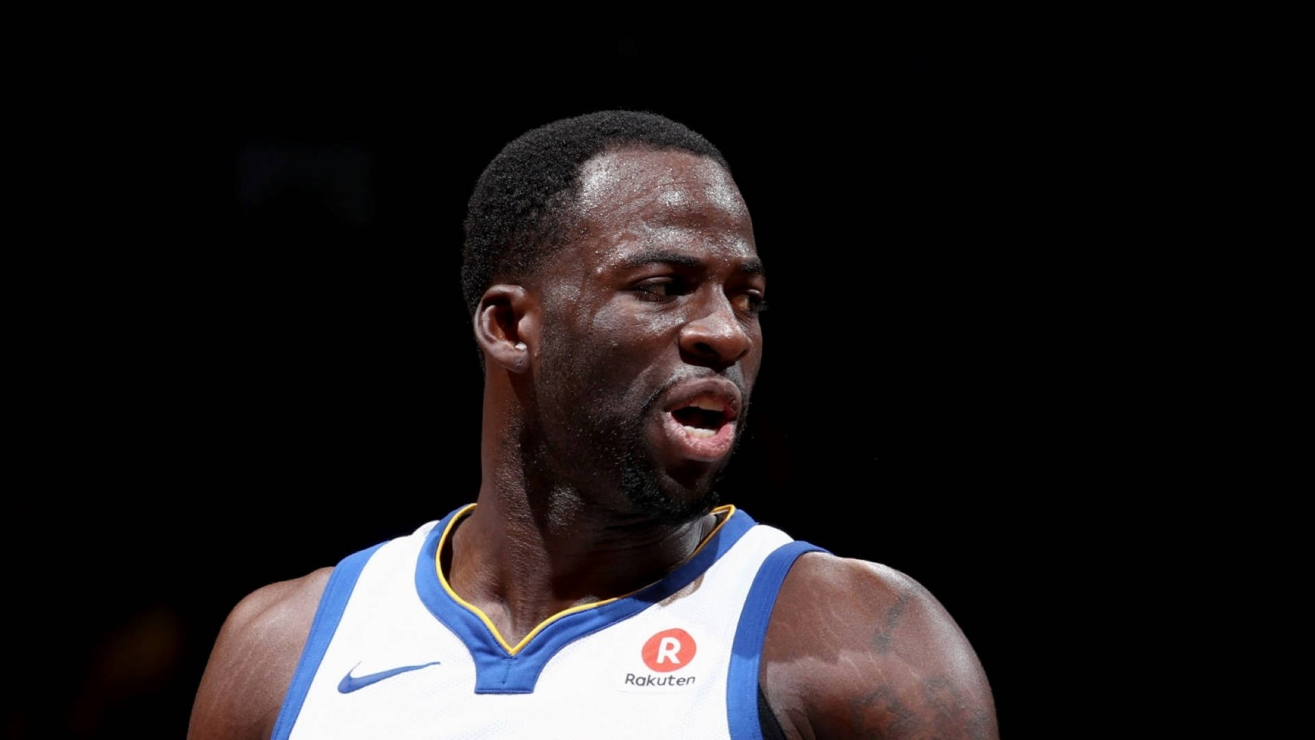 Draymond Green 桌布 壁紙 — 一位專注的籃球運動員，身穿帶有Rakuten標誌的白色和藍色球衣，背景為黑色。