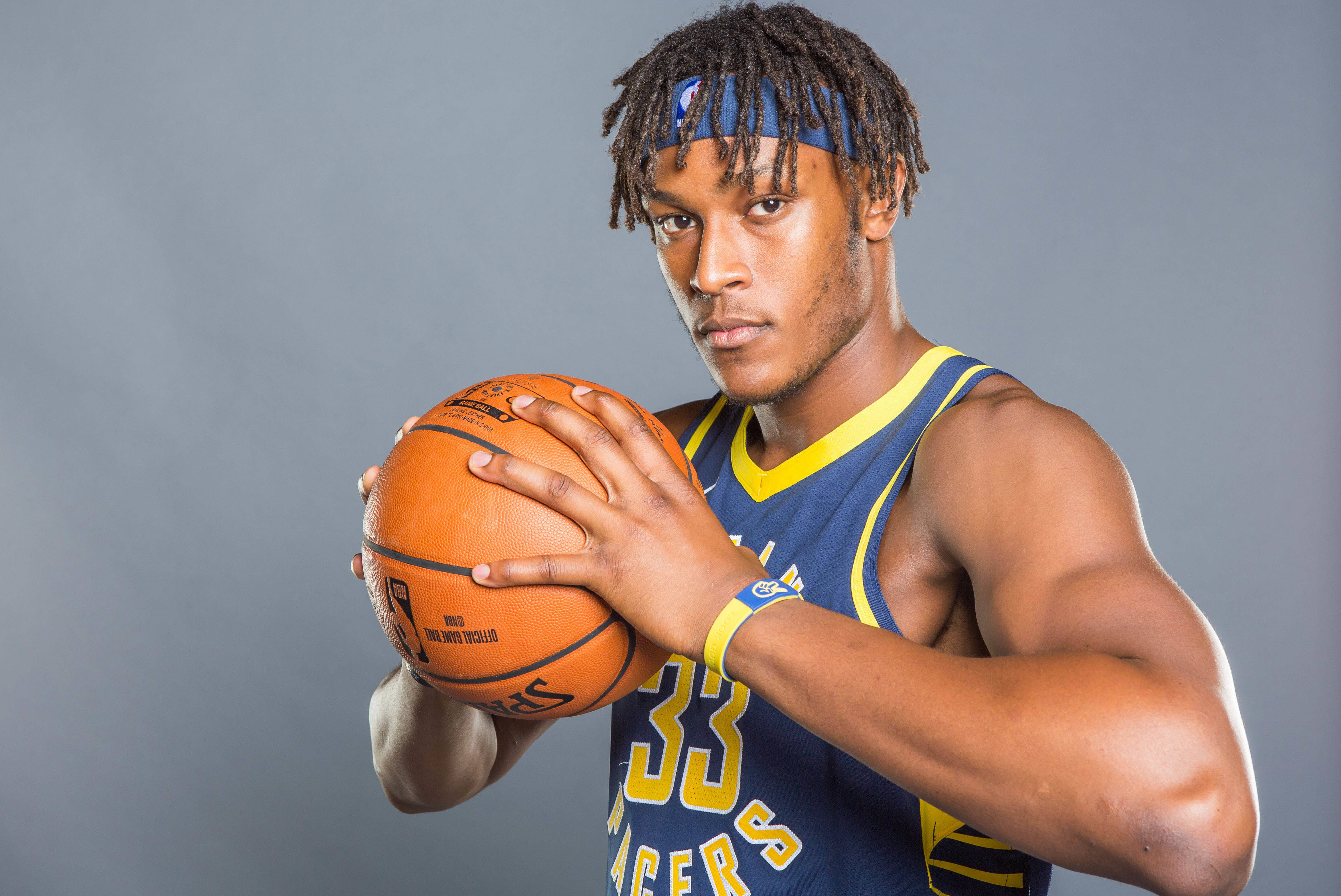 myles turner 桌布 壁紙 — 一位專注的籃球運動員，身穿藍黃色球衣，在純灰色工作室背景前拿著一個橙色籃球。