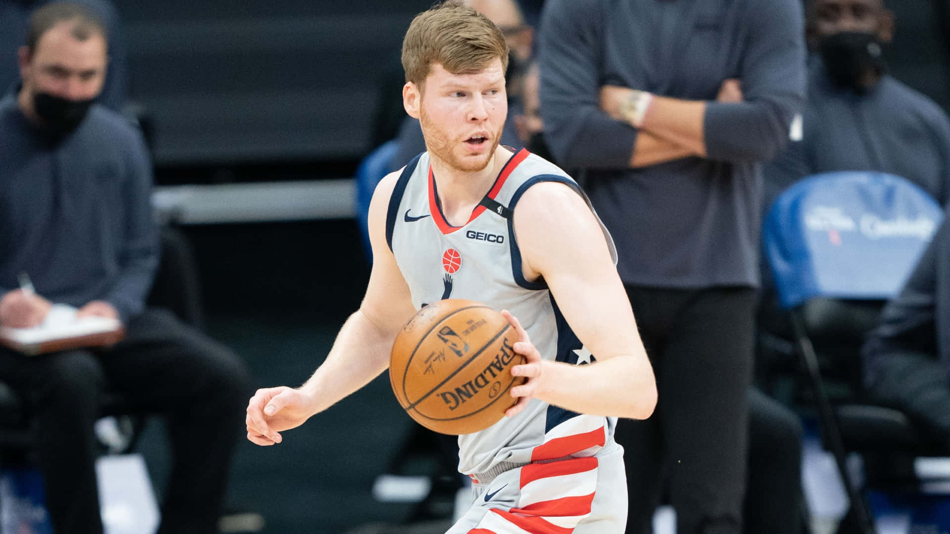NBA 桌布 壁紙 — 一位專注的籃球運動員在激烈的比賽中運球，教練們在場邊觀看。