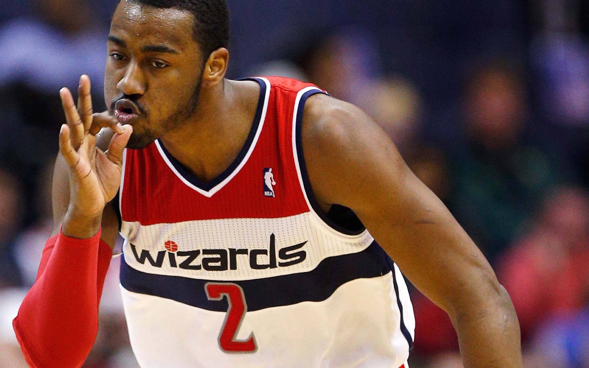 John Wall 桌布 壁紙 — 一位專注的籃球運動員穿著巫師隊球衣，在明亮的場館燈光下比賽中做出激烈的手勢。