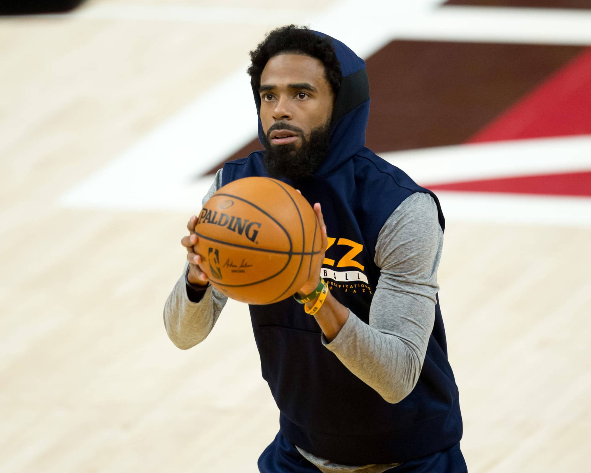 mike conley 桌布 壁紙 — 一位專注的籃球運動員穿著海軍藍連帽衫，在拋光木地板上練習時拿著一個橙色的Spalding球。