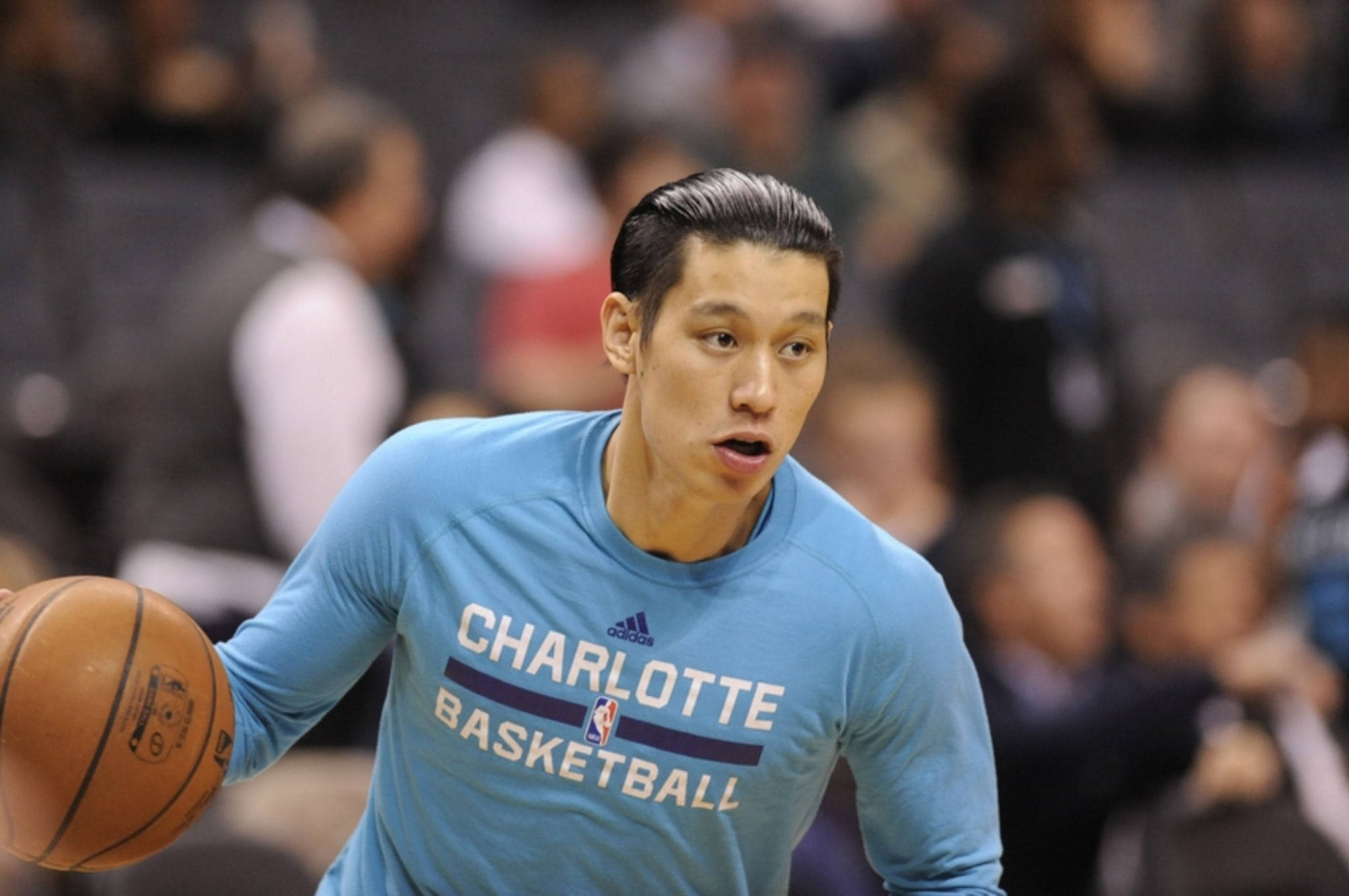Lin 桌布 壁紙 — 一位專注的籃球運動員穿著淺藍色夏洛特籃球練習球衣，在室內比賽中運球，背景有模糊的觀眾。