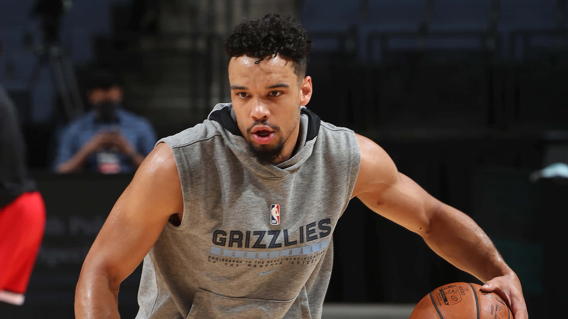 Dillon Brooks 桌布 壁紙 — 一位專注的籃球運動員穿著灰色Grizzlies無袖連帽衫，在室內練習中運球。