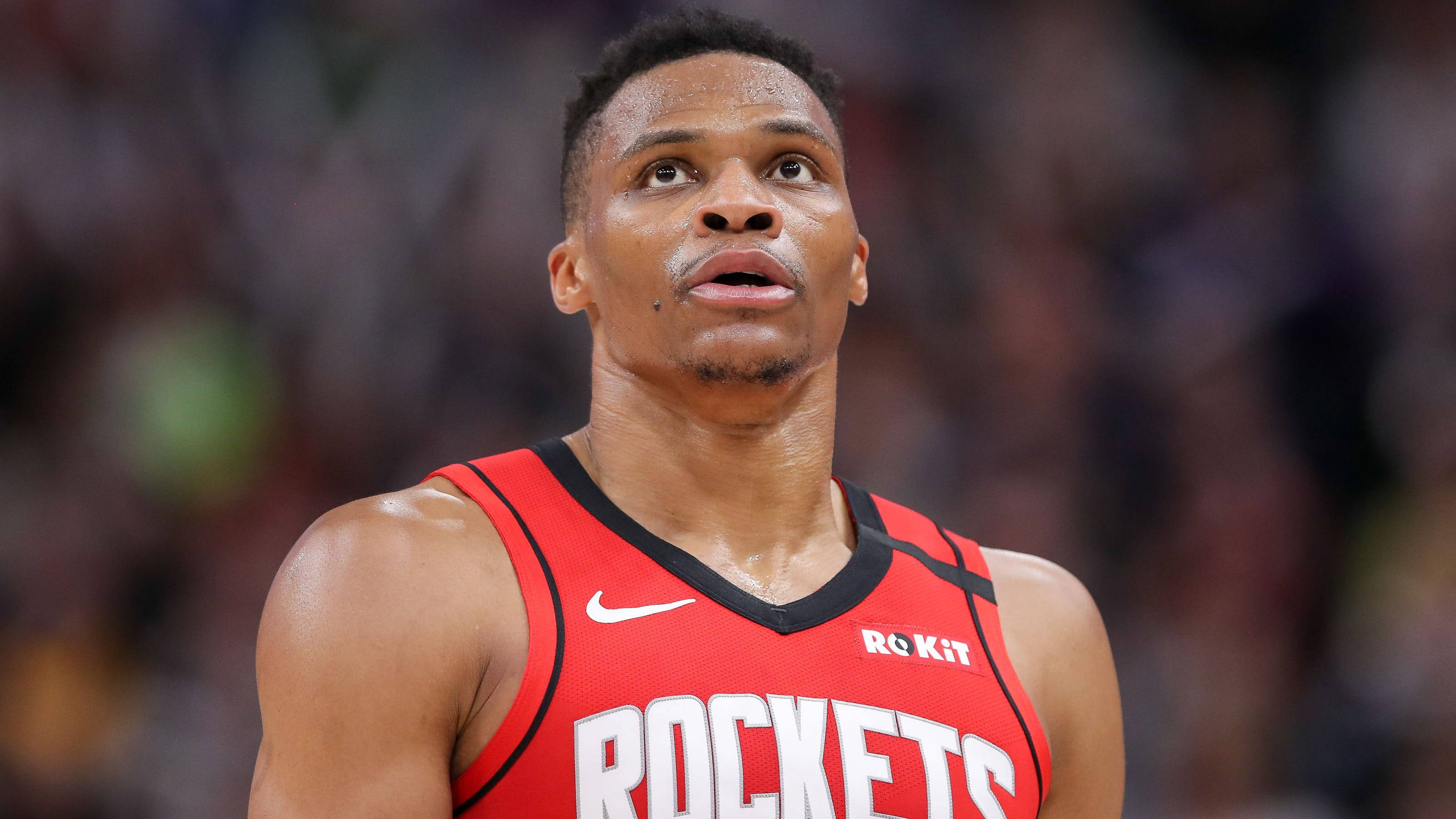 Westbrook 桌布 壁紙 — 一位專注的籃球運動員穿著紅色火箭隊球衣，在明亮的場館燈光下於激烈的比賽中向上凝視。