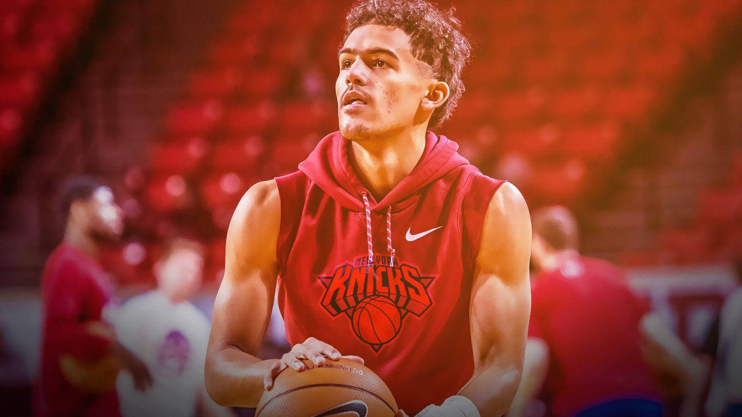 Trae Young 桌布 壁紙 — 一位專注的籃球運動員穿著紅色紐約尼克隊無袖連帽衫，在模糊的隊友和紅色座位的體育館中拿著球。